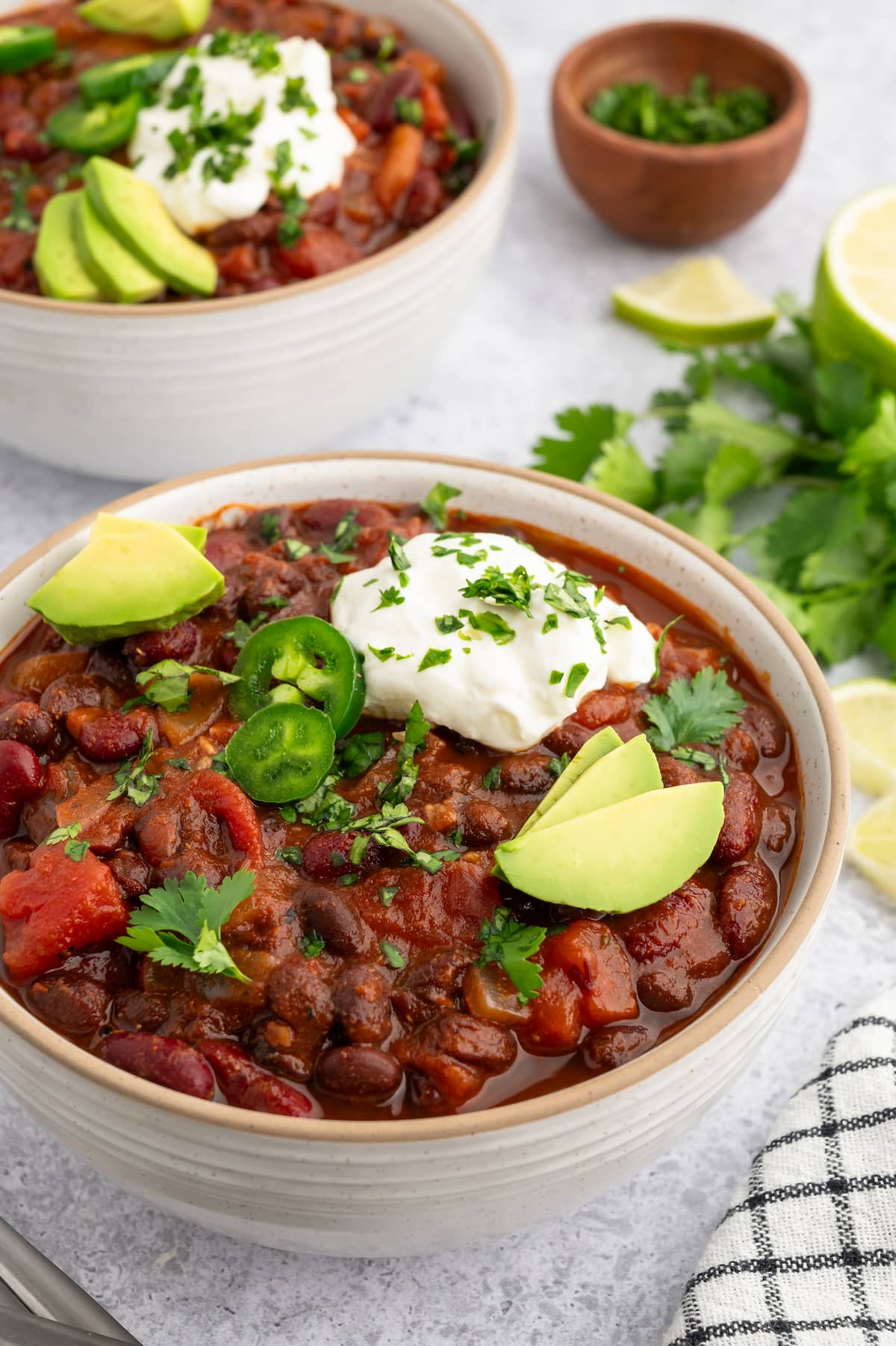 A bowl of vegan chili topped with dairy-free sour cream, avocado and jalapeno slices.