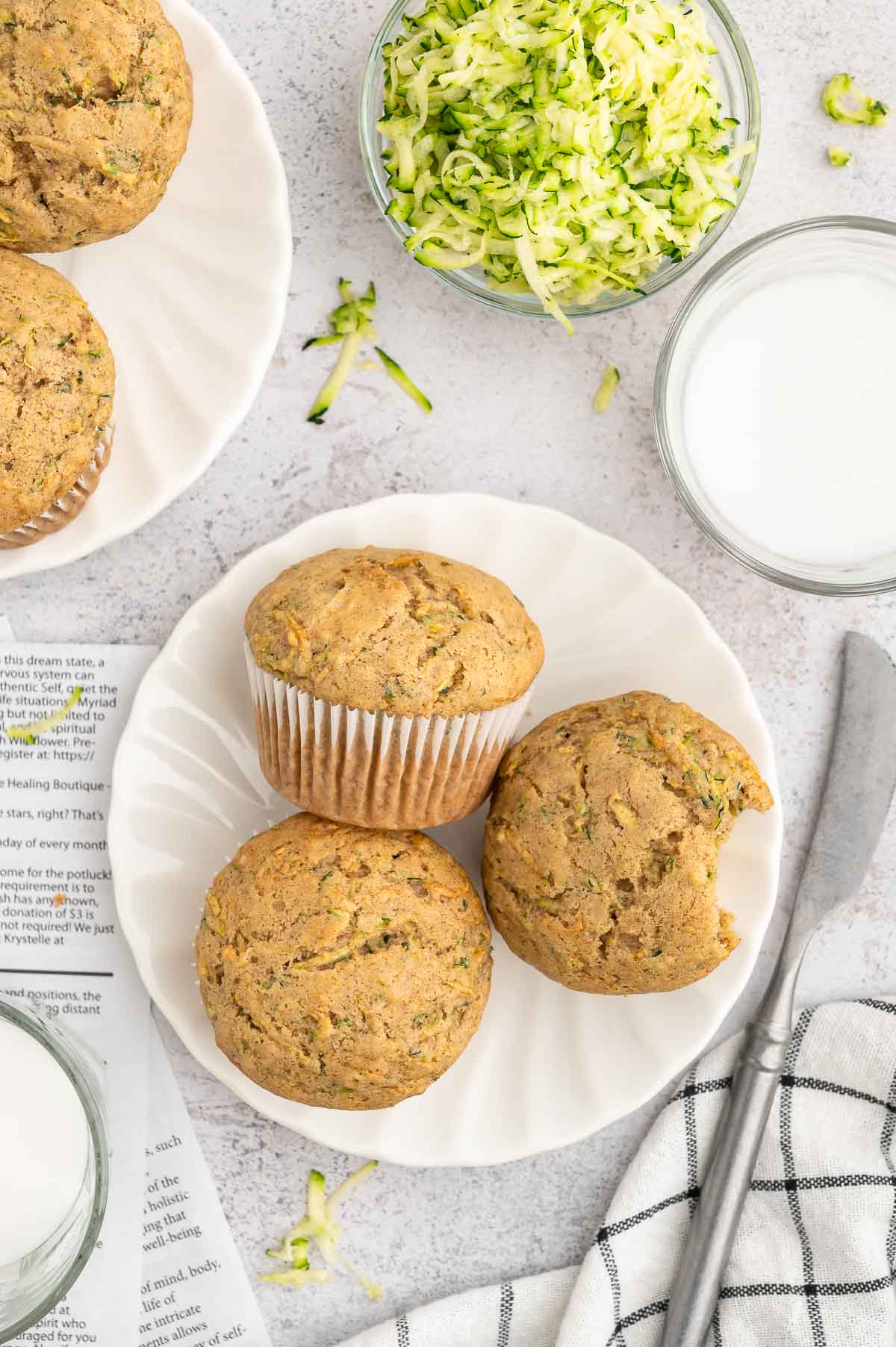 Three vegan zucchini muffins on a plate with one that's had a bite taken out of it.