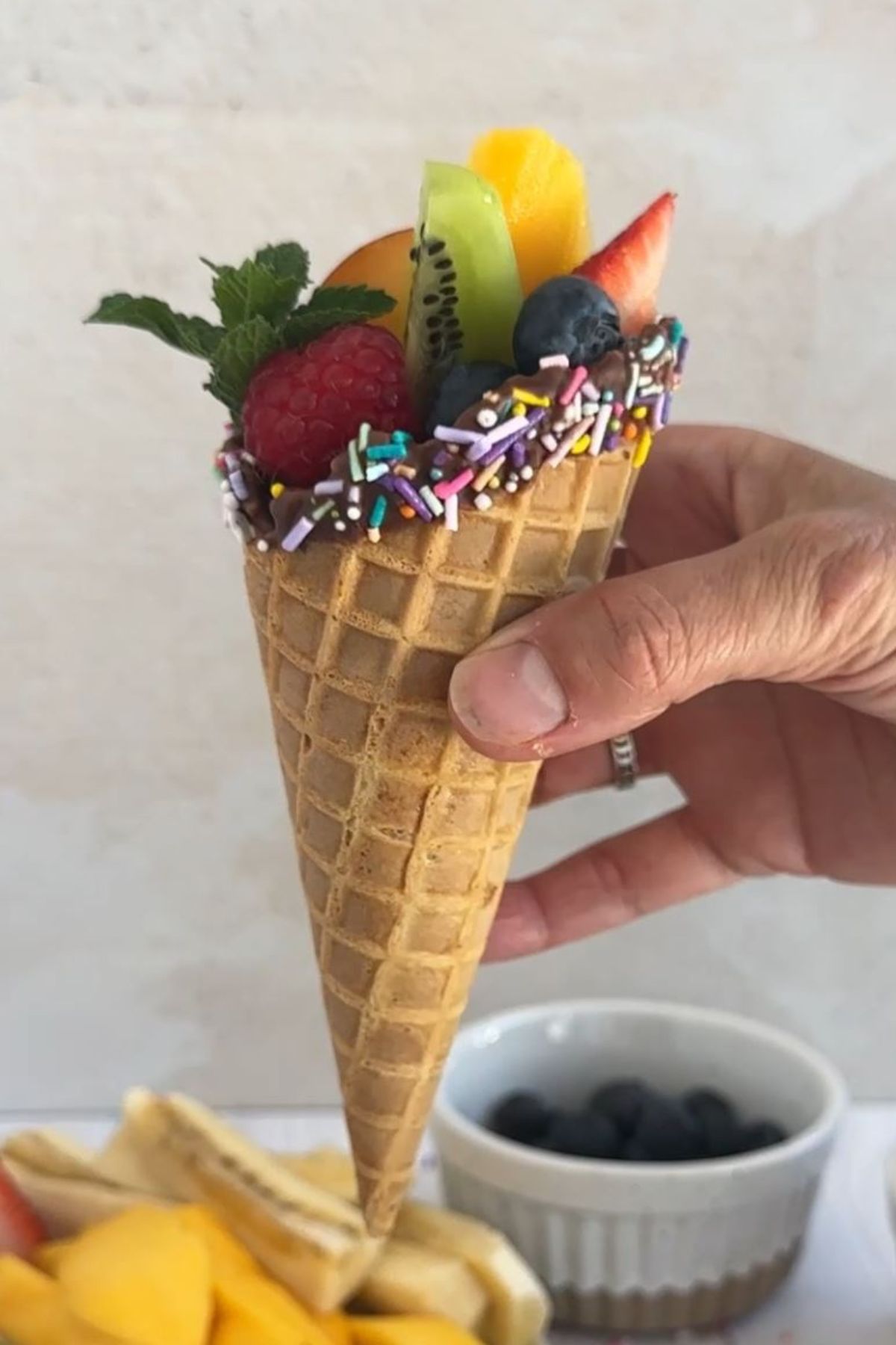 An assembled fruit cone with chocolate nd sprinkles.