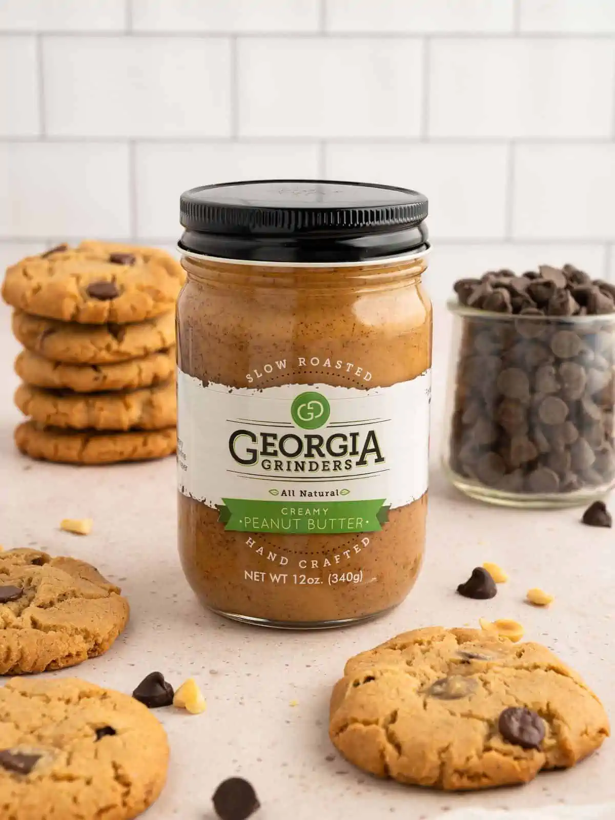 Creamy natural peanut butter from Georgia Grinders brand surrounded by vegan peanut butter cookies.