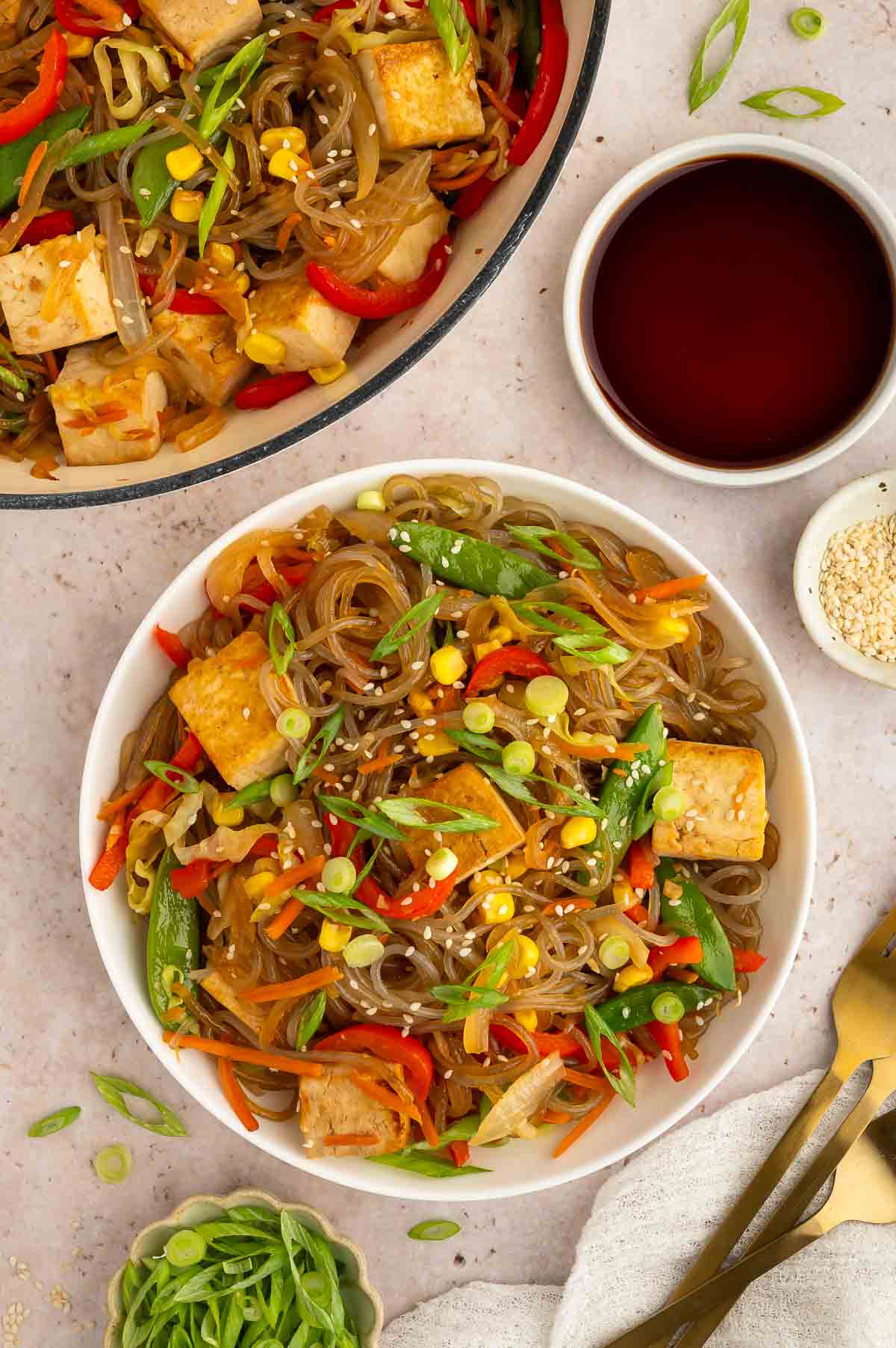 A bowl of glass noodles and tofu with veggies, served on a plate.