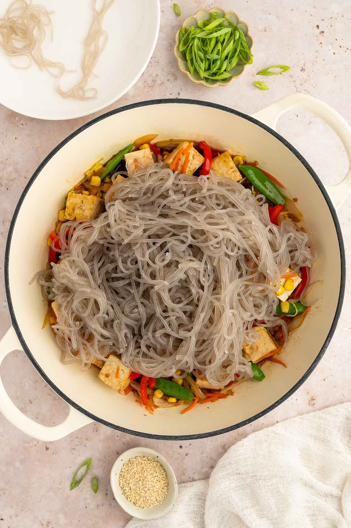 A pan with tofu and veggies with glass noodles on top.