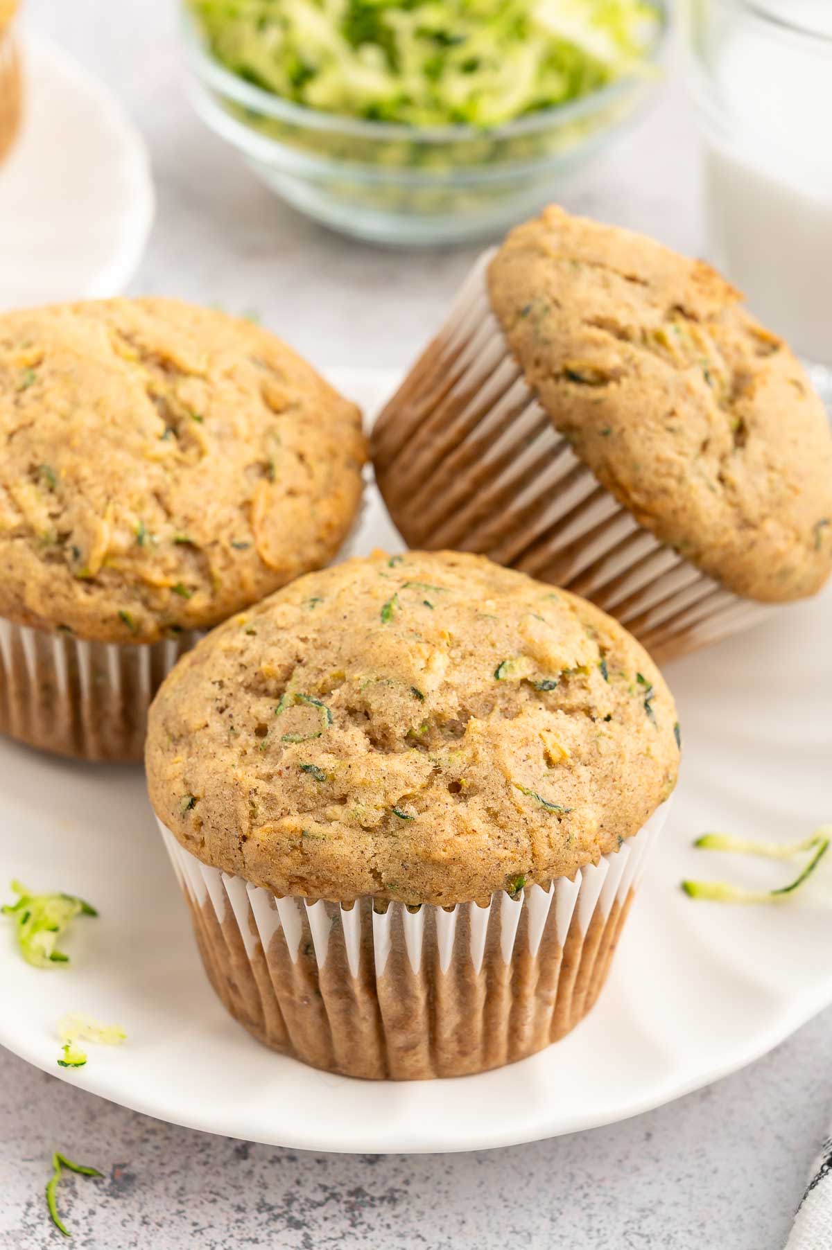 Three vegan zucchini muffins with liners on a plate.