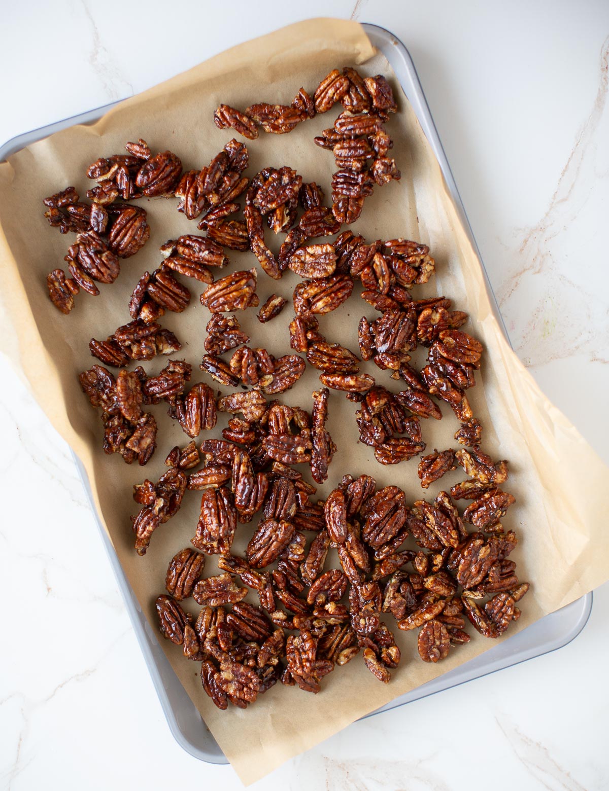 Candied pecans cooling on a parchment lined baking tray.