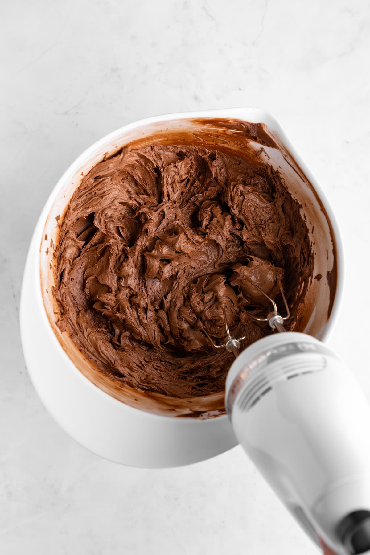 Vegan chocolate frosting in a mixing bowl being whipped with a handheld mixer.