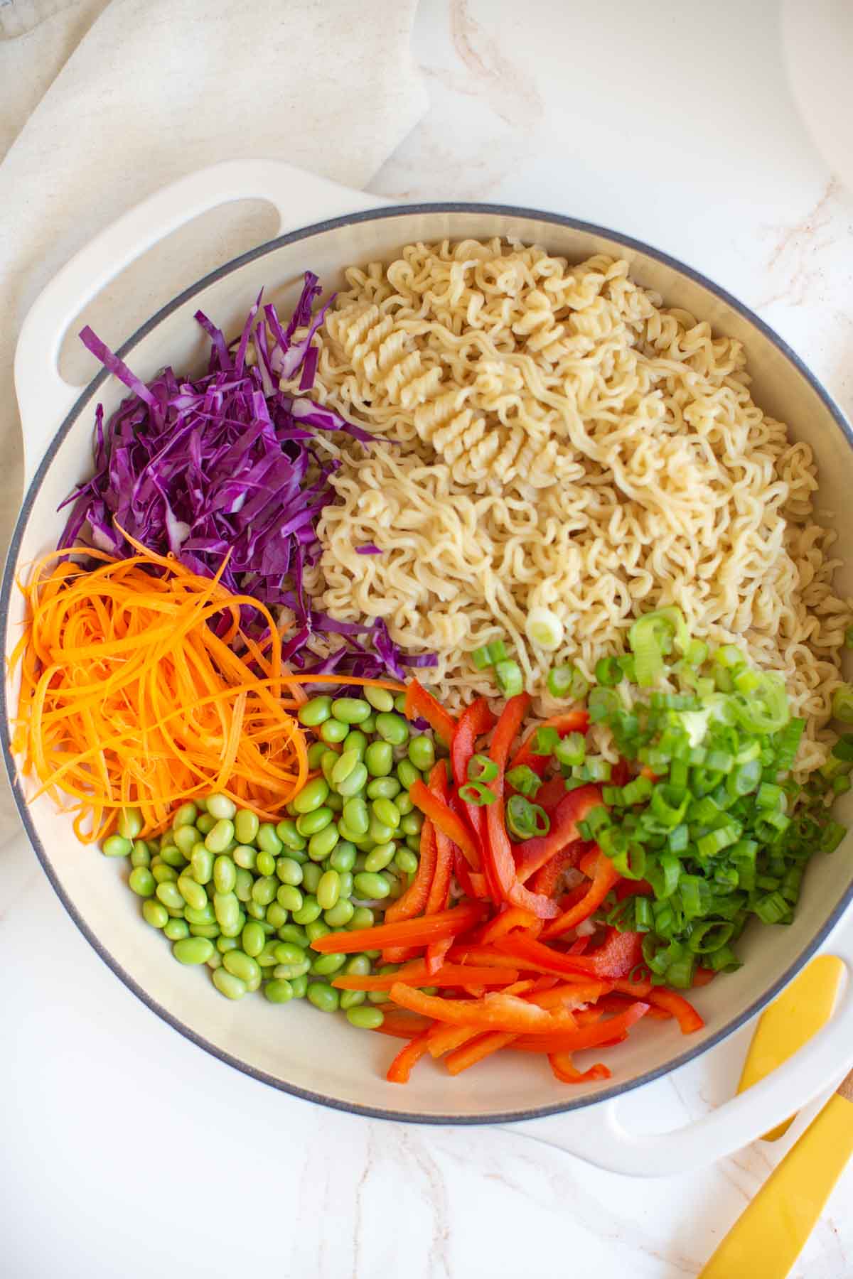 Ingredient flatlay with cooked ramen noodles, green onions, red bell pepper, edamame, carrots, and cabbage.