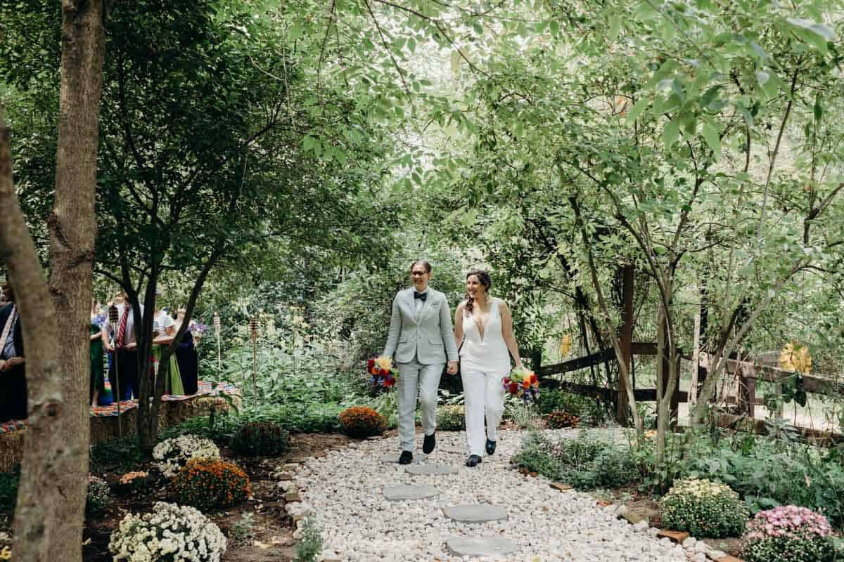 Queer couple walking down a handmade woodland path at their vegan wedding.