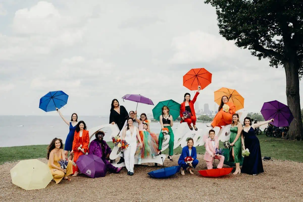 A rainbow wedding party, wearing colorful outfits and umbrellas.