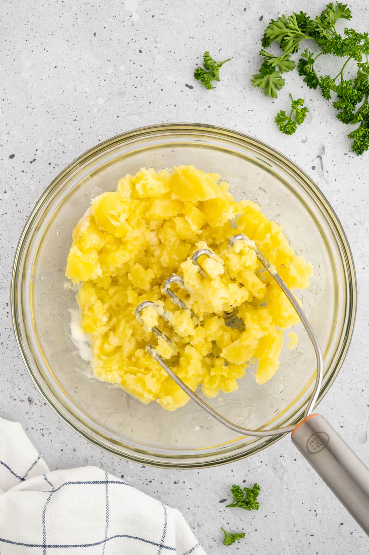 A glass bowl with mashed yukon gold potatoes using a potato masher.