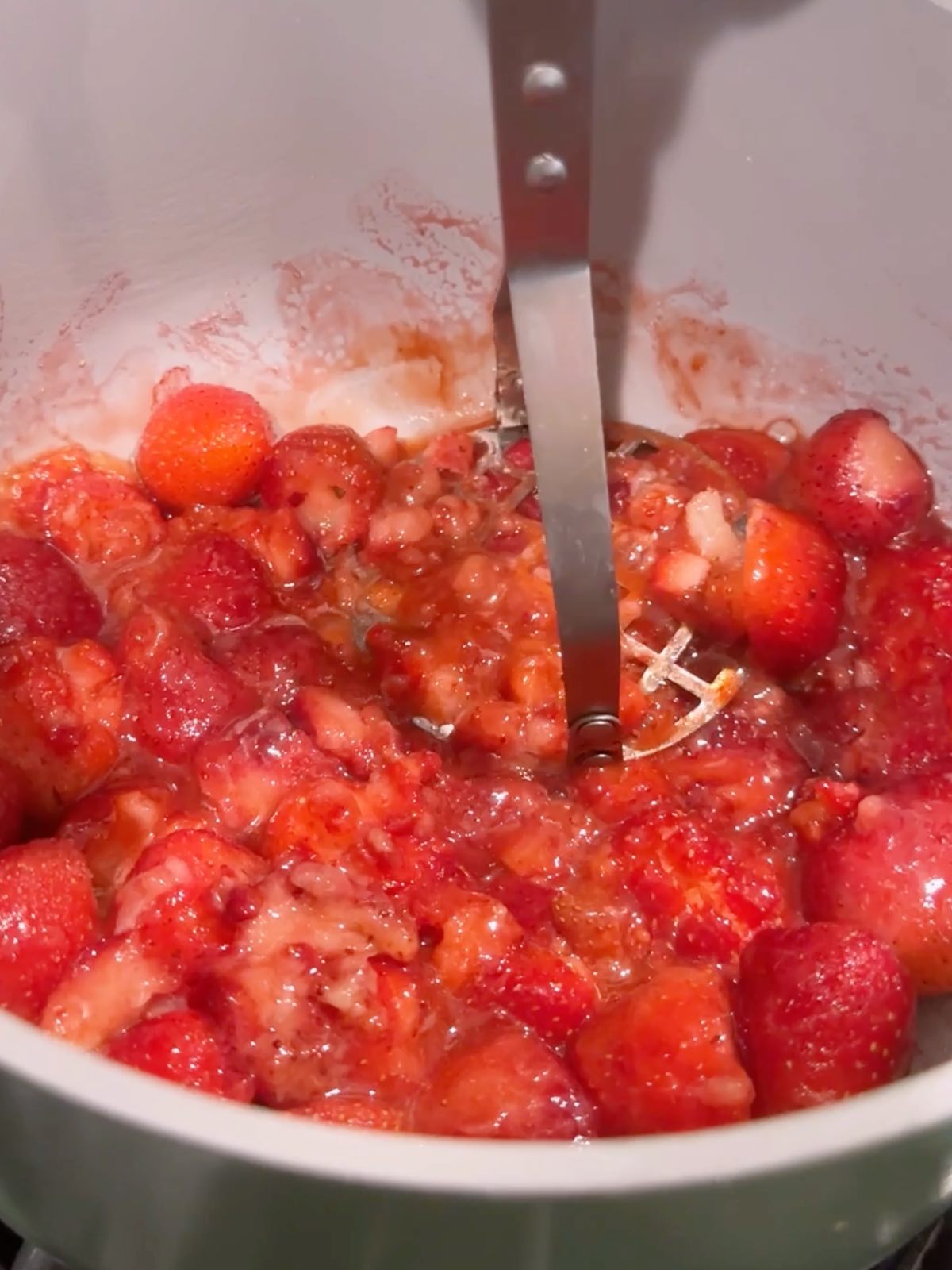 Mashing strawberries in a pot with a potato masher.