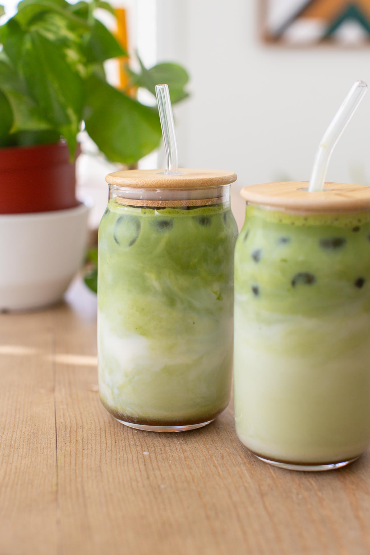 Two glasses of iced matcha lattes with glass straws.