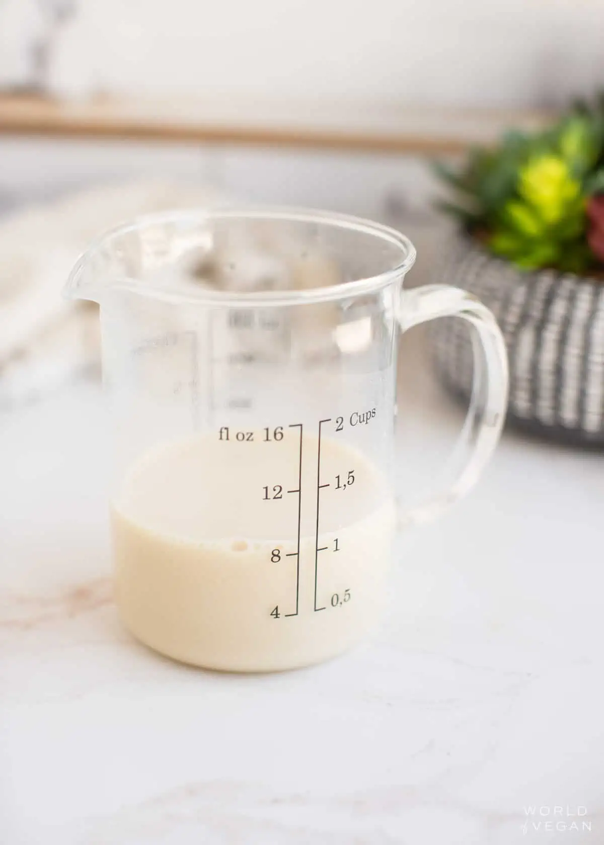A glass measuring cup filled with non-dairy milk.