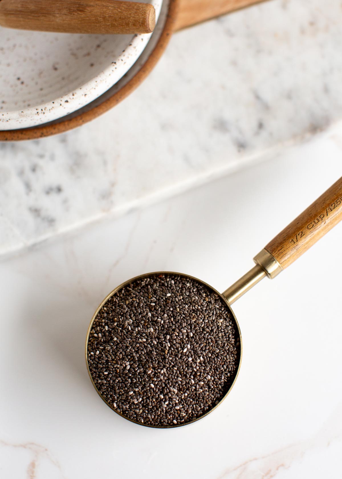 Half cup of chia seeds in a gold measuring cup with a wooden handle.