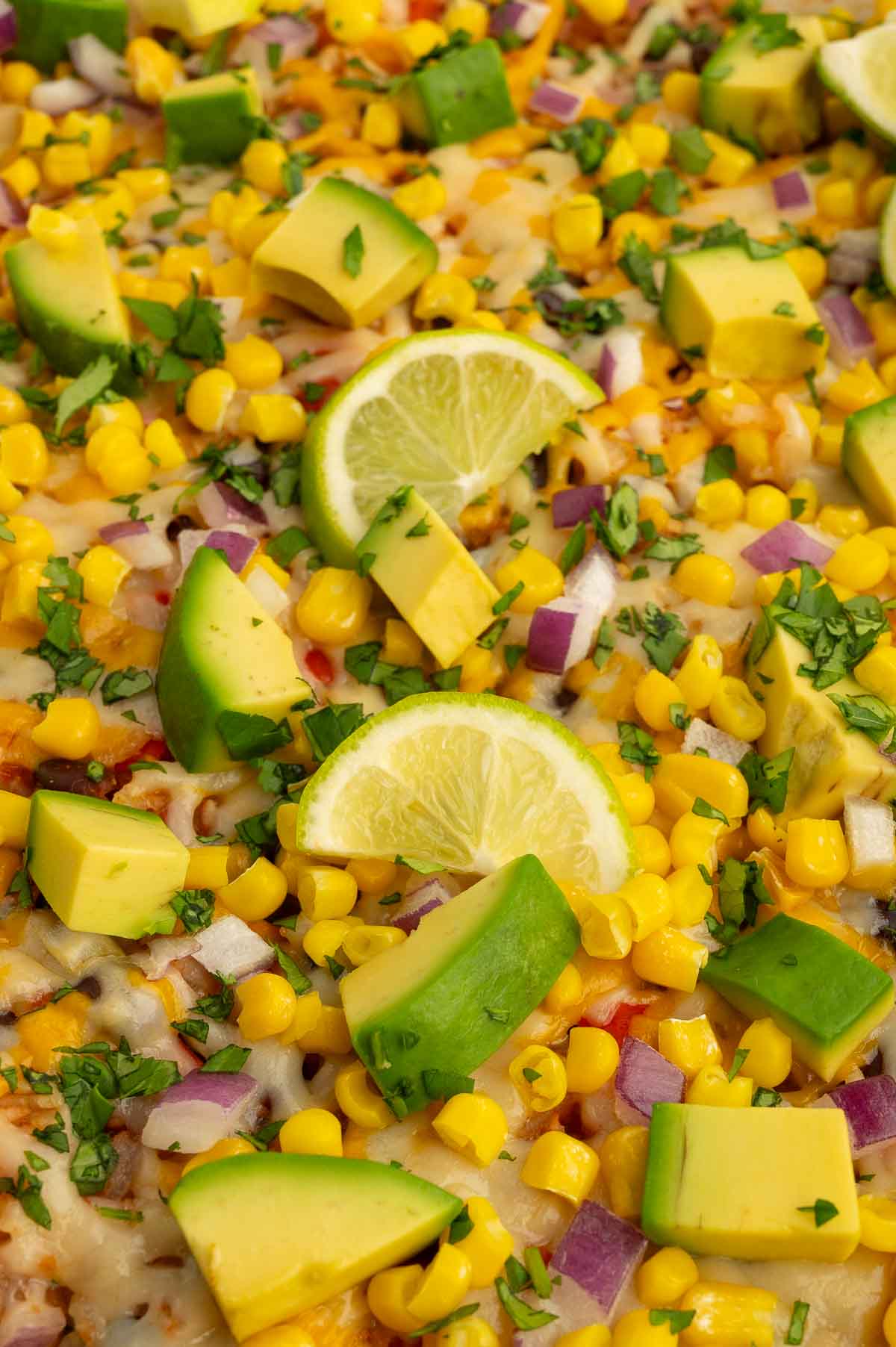 Mexican bean and rice casserole topped with red onion, corn, avocado, cilantro, and lime slices.