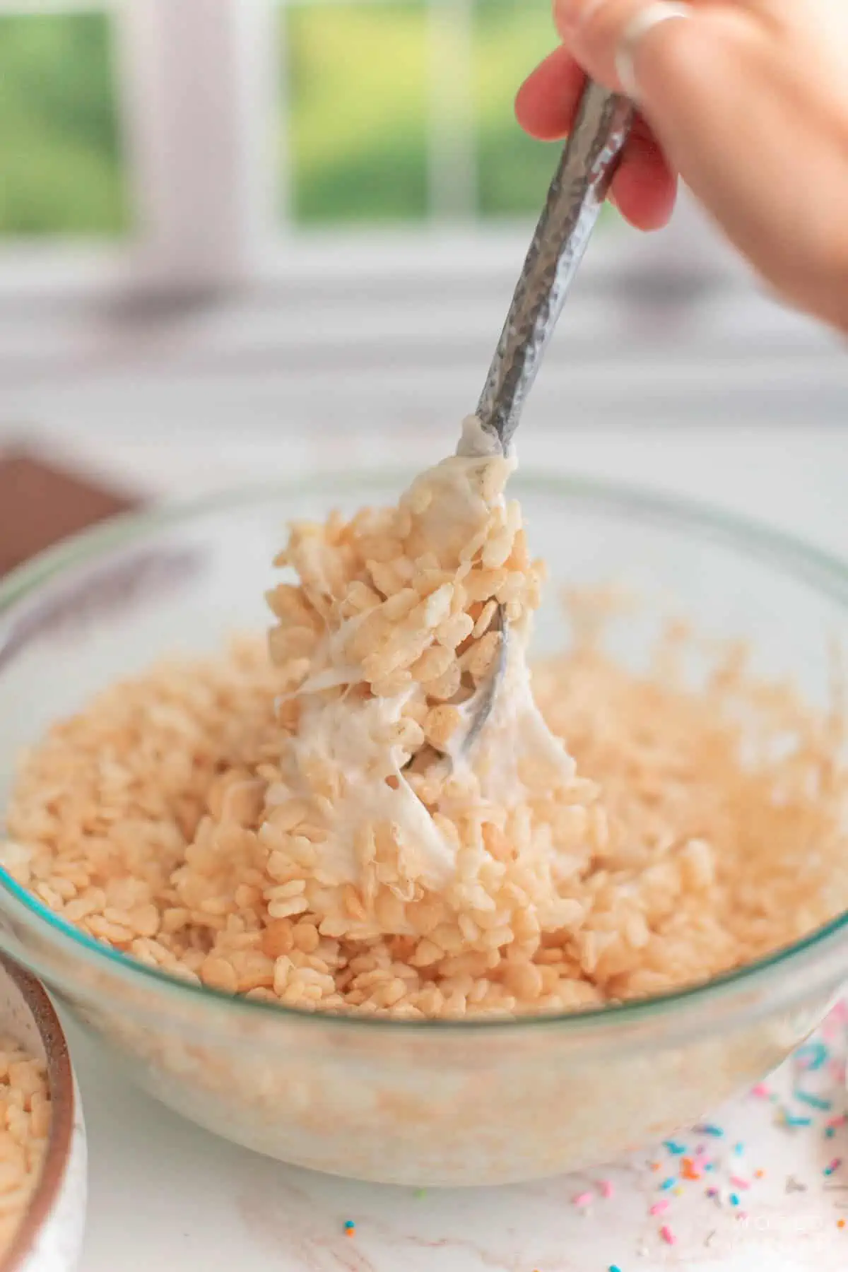 A spoon mixing together rice krispies cereal with melted marshmallows.