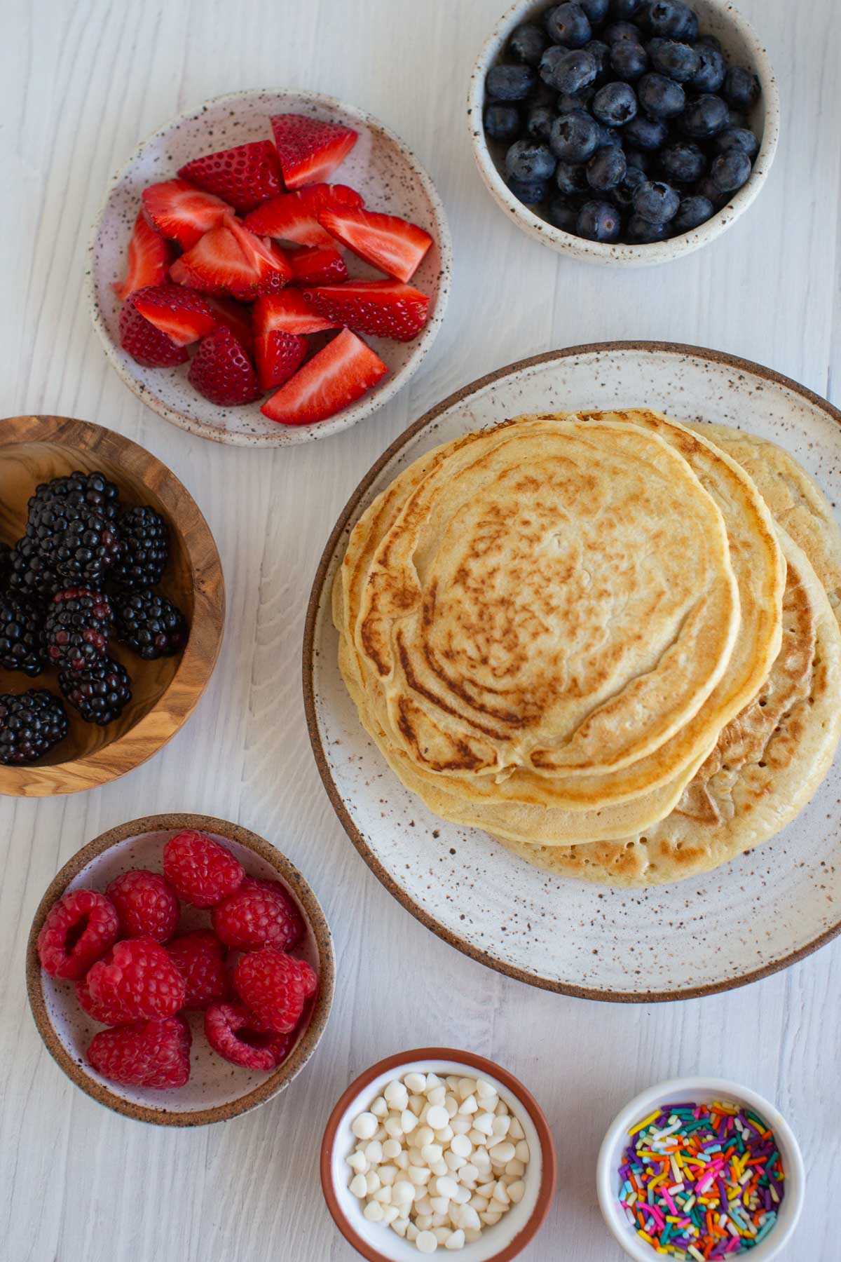 A stack of pancakes surrounded by different toppings.