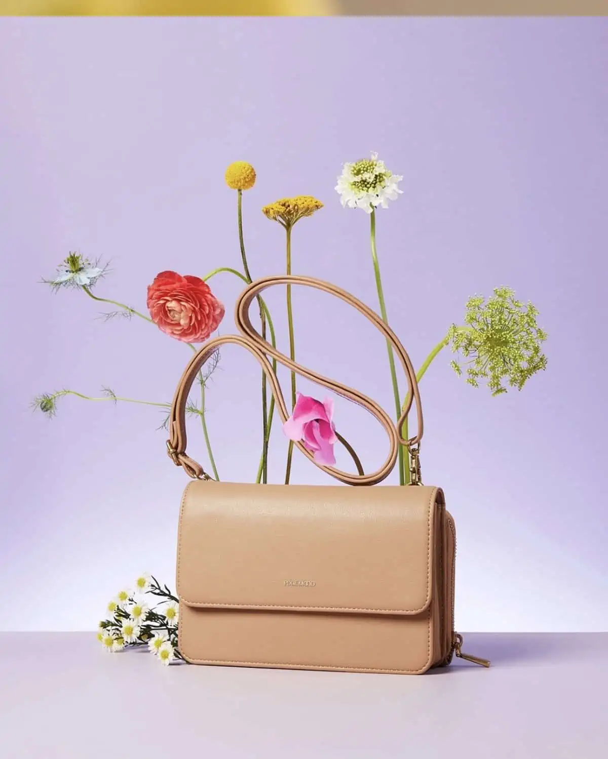 Camel tan small vegan purse from Pixie Mood surrounded by colorful wildflowers on a purple background.