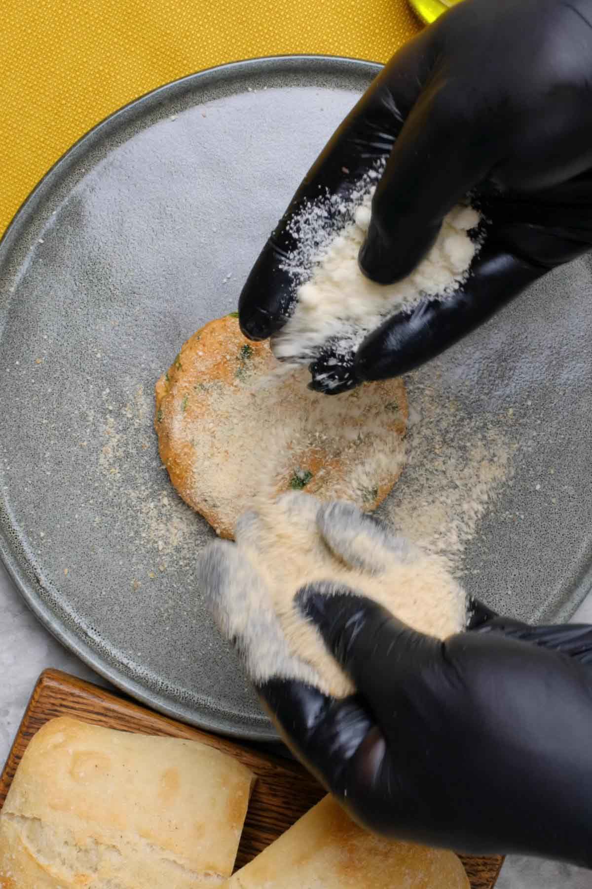 A formed pizza burger being coated in breadcrumbs.