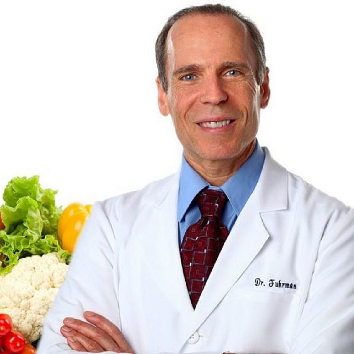Headshot photo of Dr. Joel Fuhrman in a white lab coat embroidered with his name with fruit and vegetables behind him.