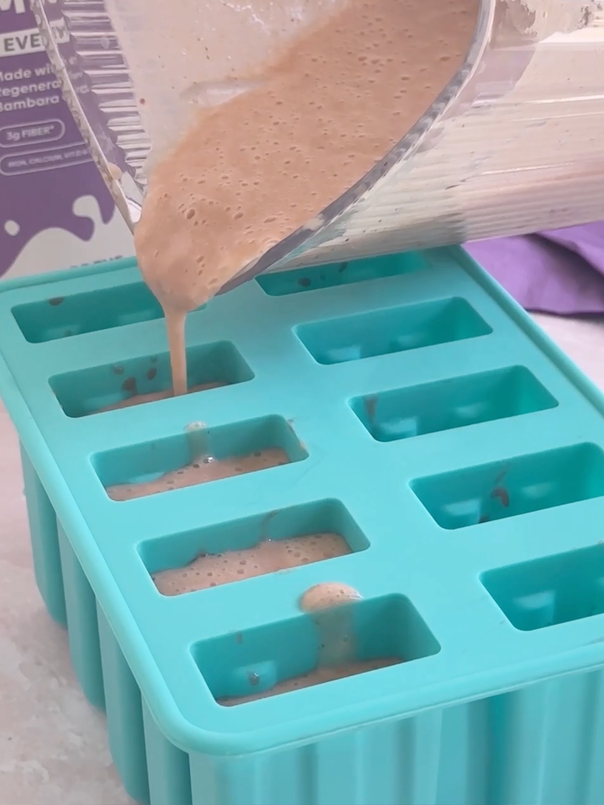 Pouring banana strawberry popsicle mixture into blue 10-slot silicone popsicle molds.