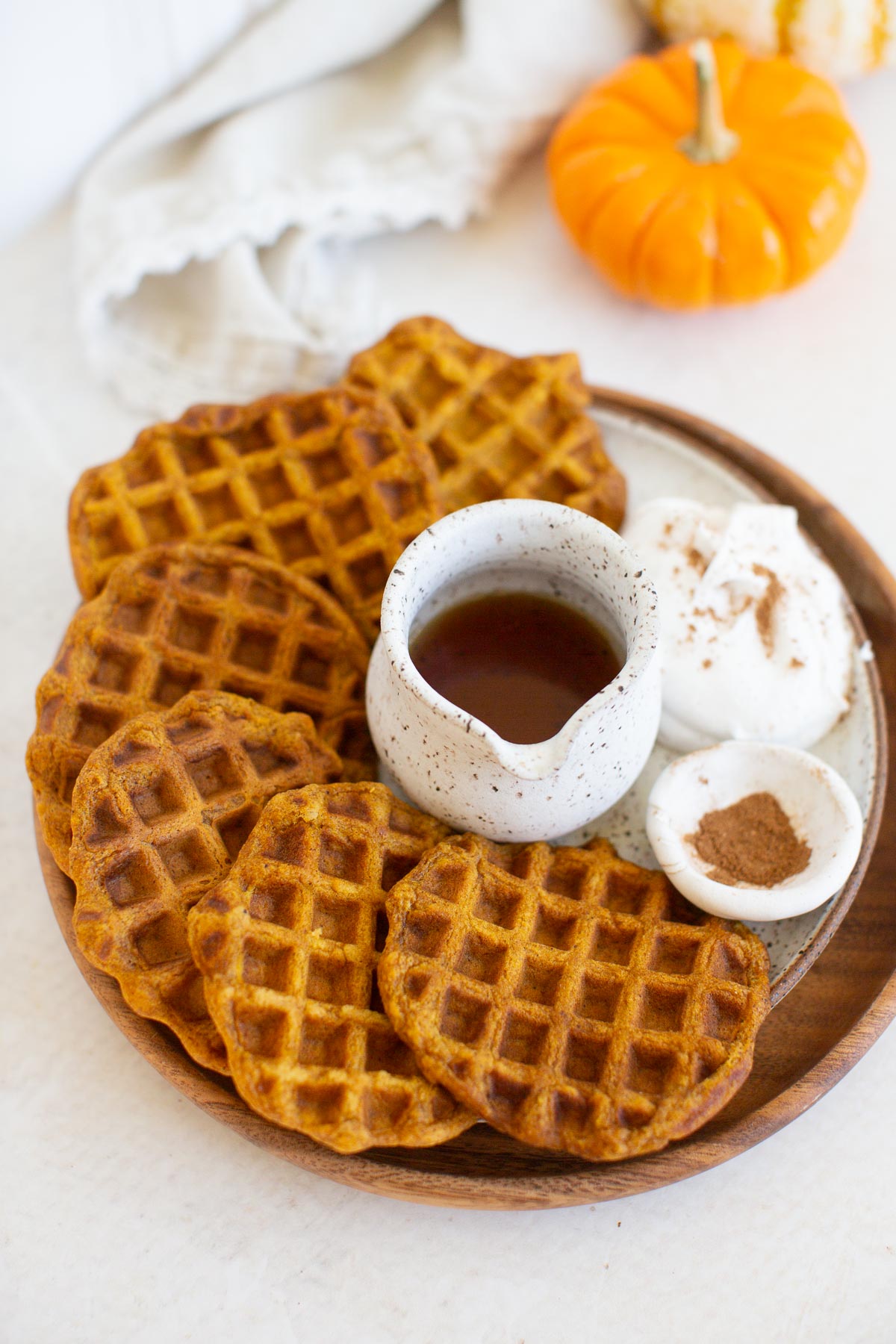 A platter of vegan pumpkin spice waffles with a side of vegan whipped cream, maple syrup, and extra pumpkin pie spice.