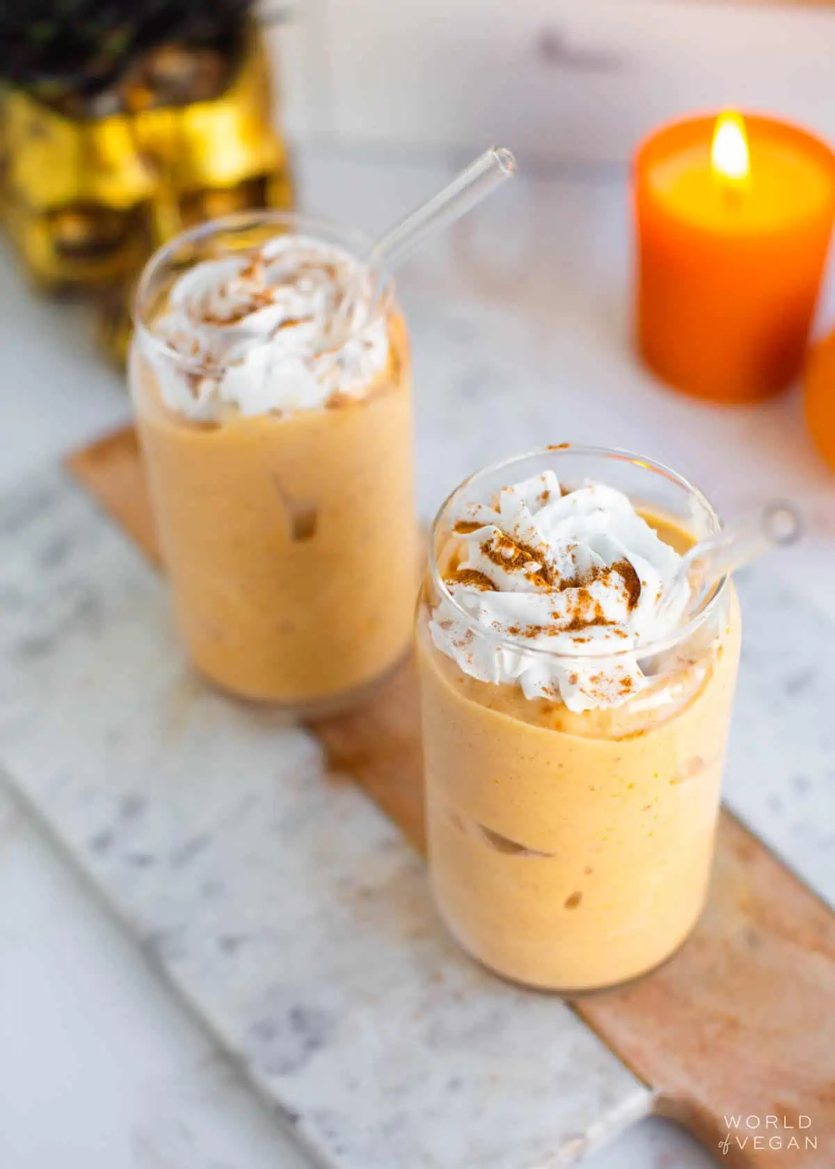 Two glasses of pumpkin pie milkshake topped with vegan whipped cream and sprinkled with pumpkin pie spice.