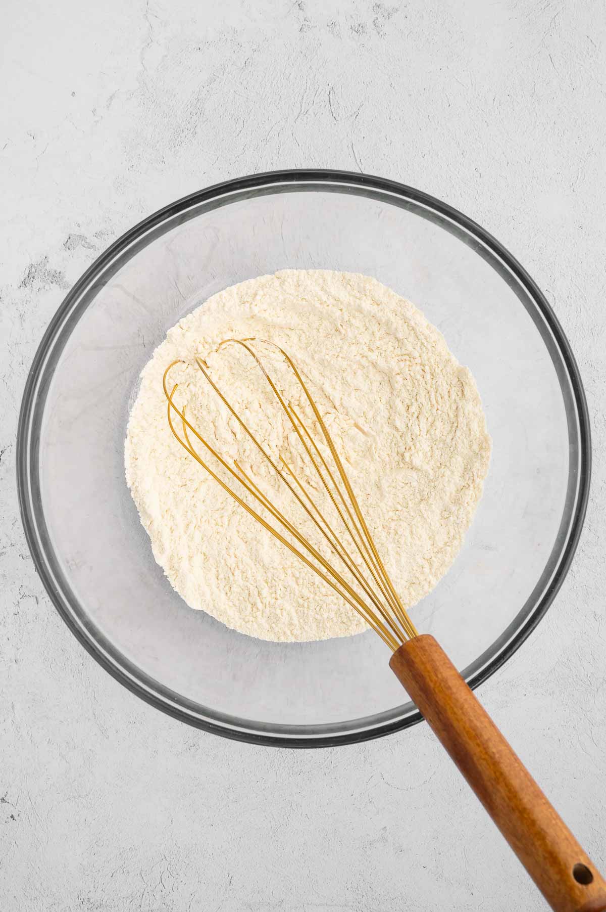 A bowl of flour with a whisk.