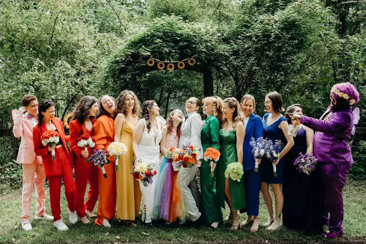Rainbow wedding party photo in colorful forest setting.