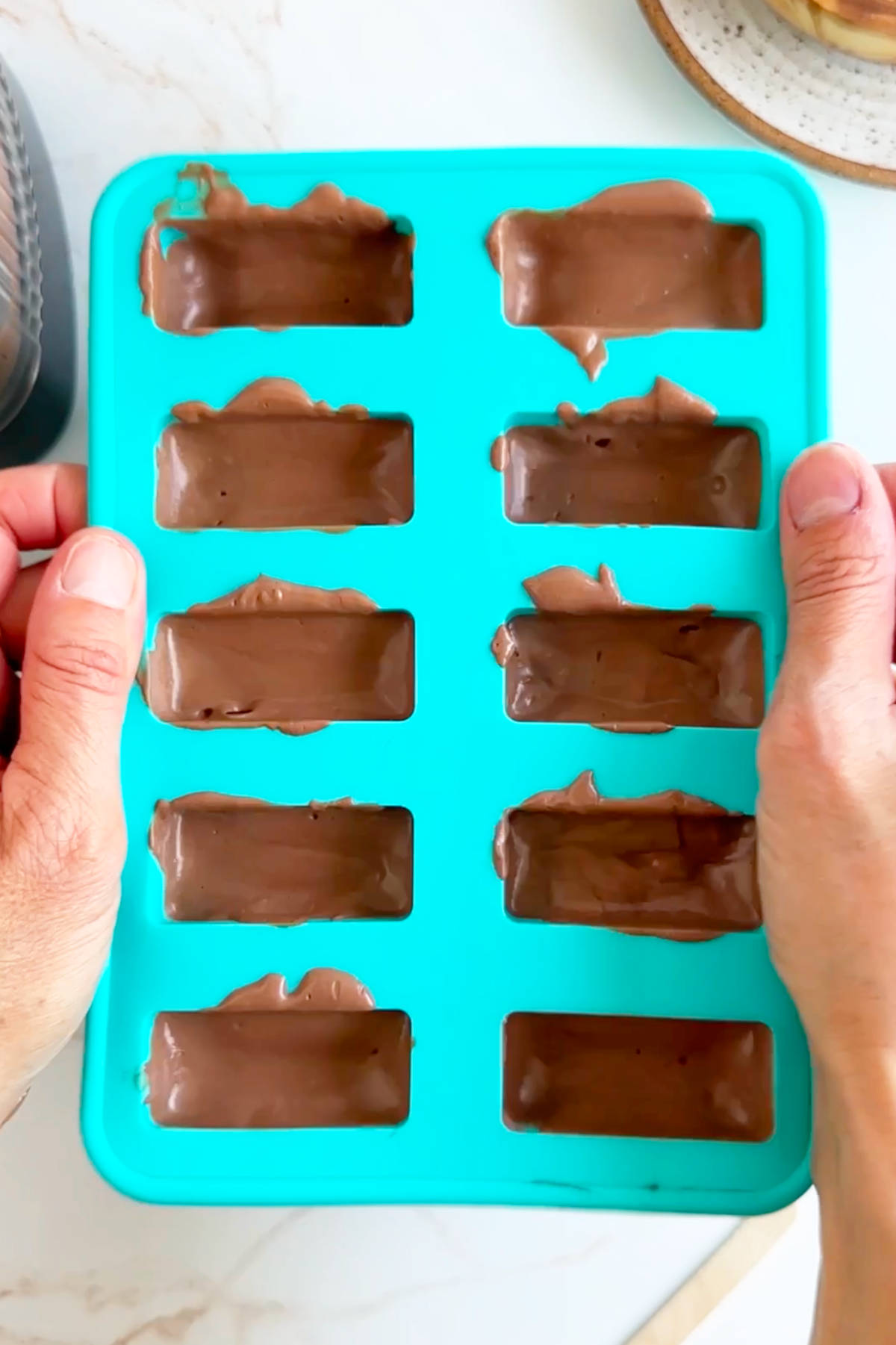 Hands holding the sides of the popsicle mold to tap it out the countertop and release air bubbles.