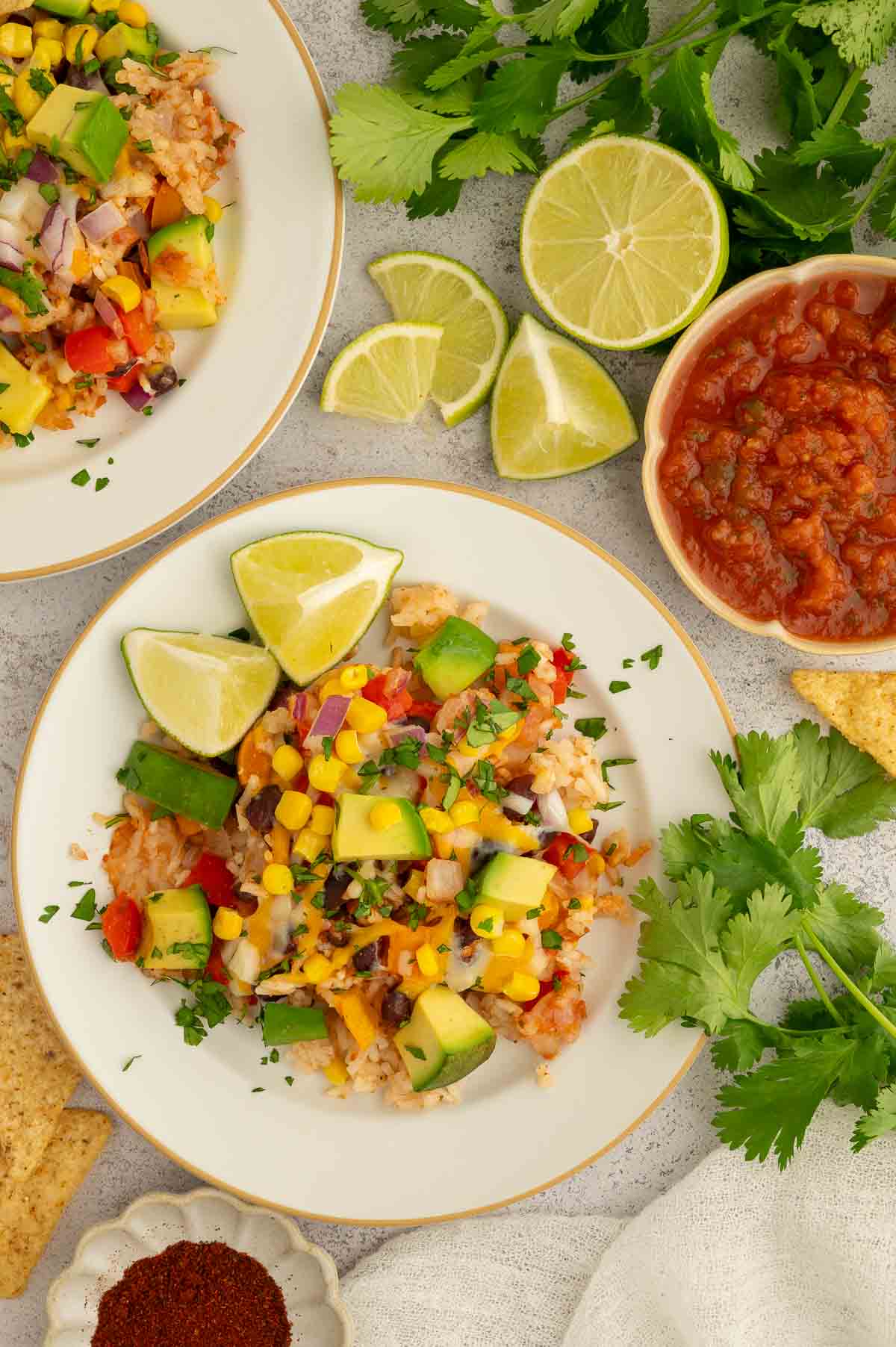A serving of rice and bean casserole on a plate with lime slices and a bowl of salsa next to it.