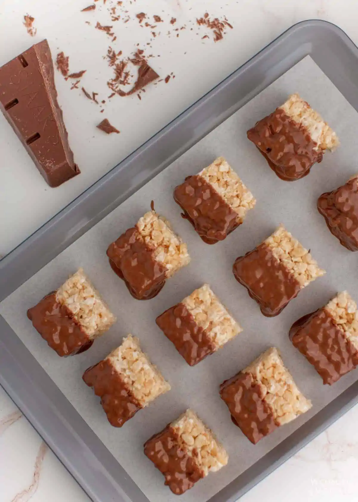 Chocolate covered rice krispies treats on baking sheet with parchment paper.