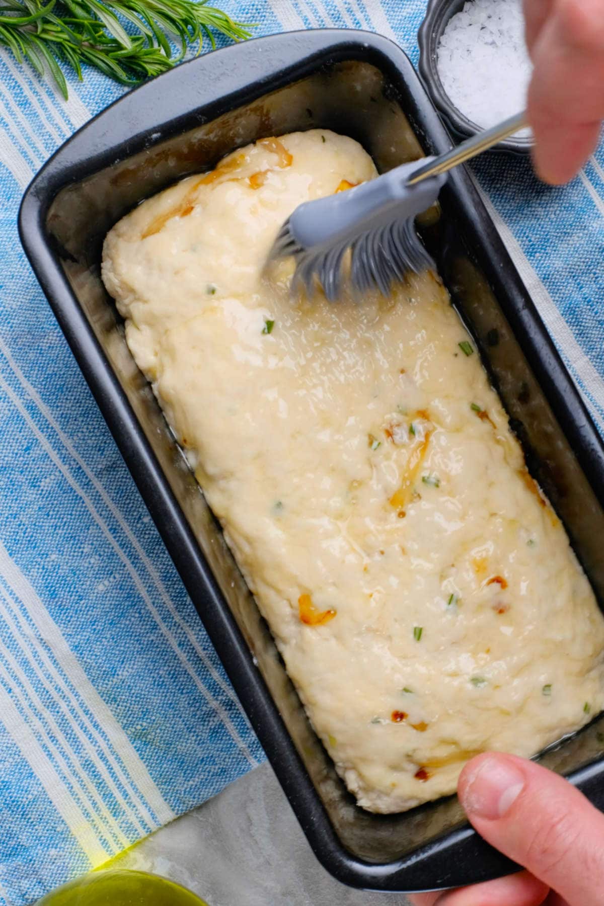 Rosemary beer bread dough added to the loaf pan with a basting brush adding some melted butter on top.