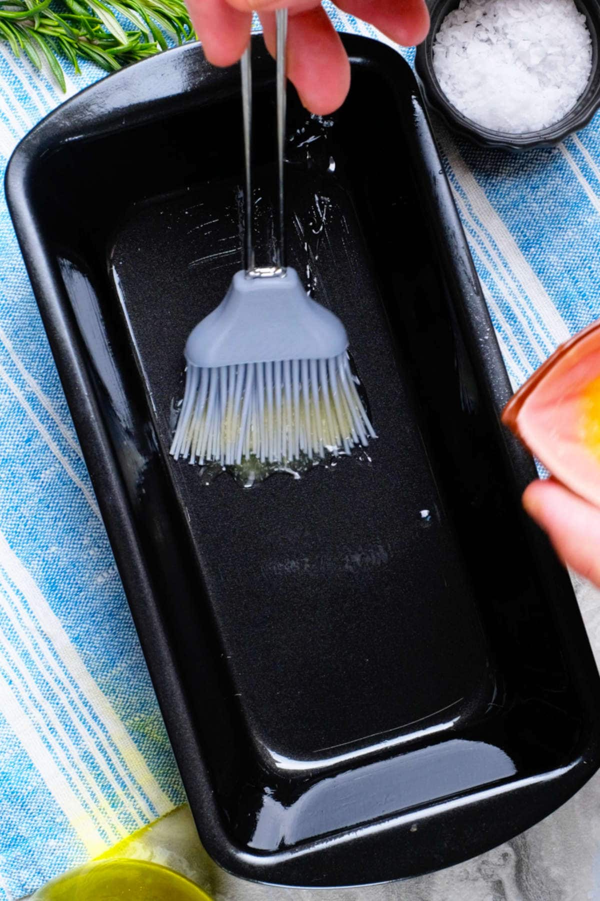 A basting brush brushing oil in a loaf pan.