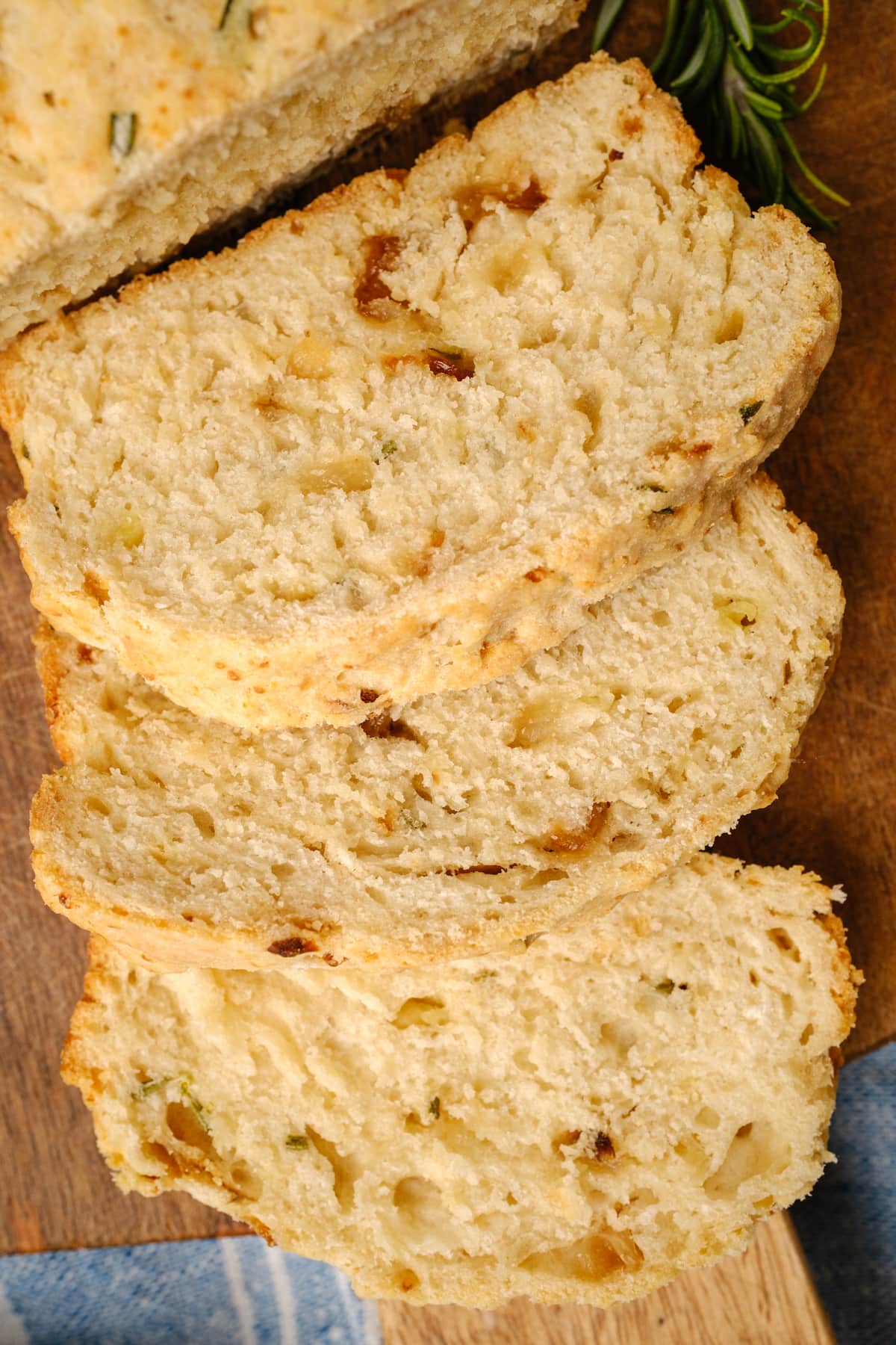Slices of rosemary bread laying on a wooden cutting board.