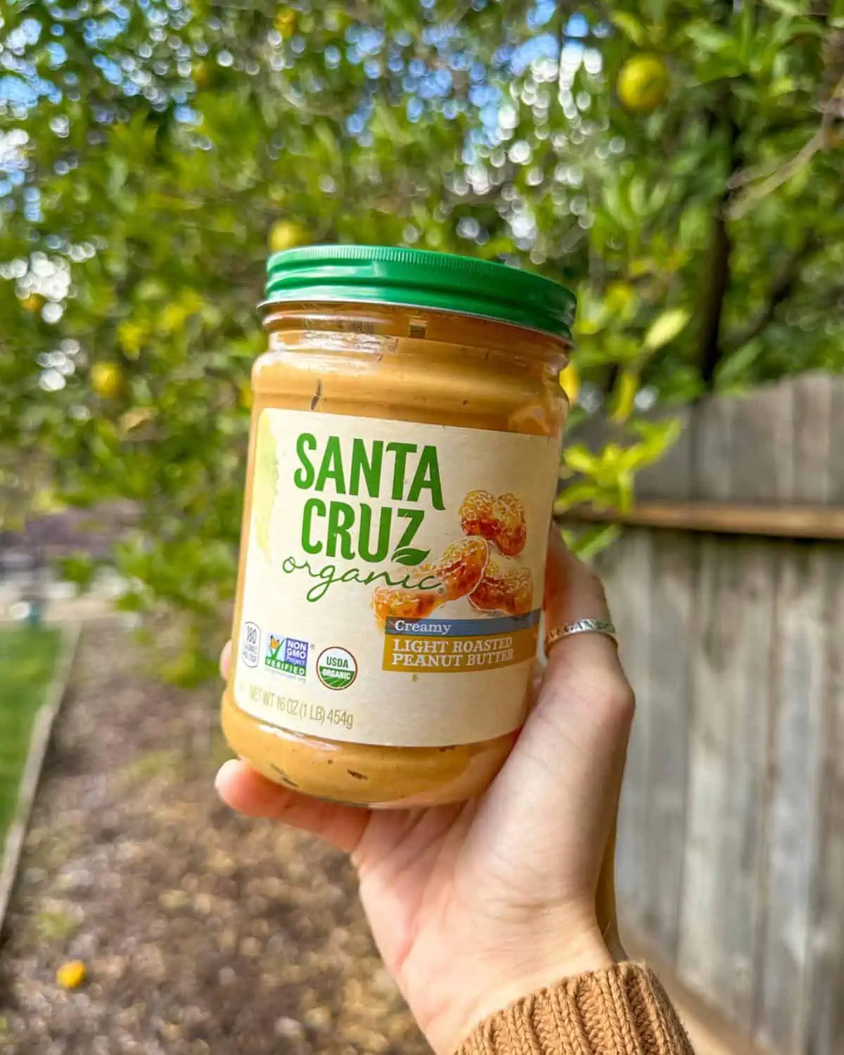 Woman's hand holding out a jar of Santa Cruz Organic creamy vegan peanut butter.