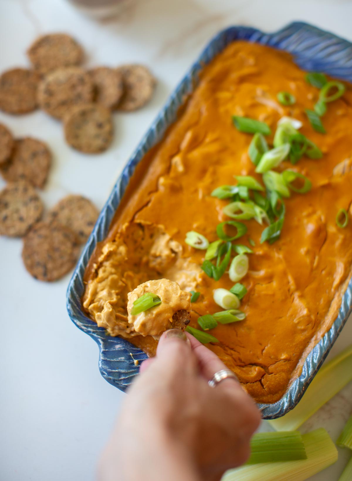 A hand using a cracker to scoop up some vegan buffalo chicken dip.