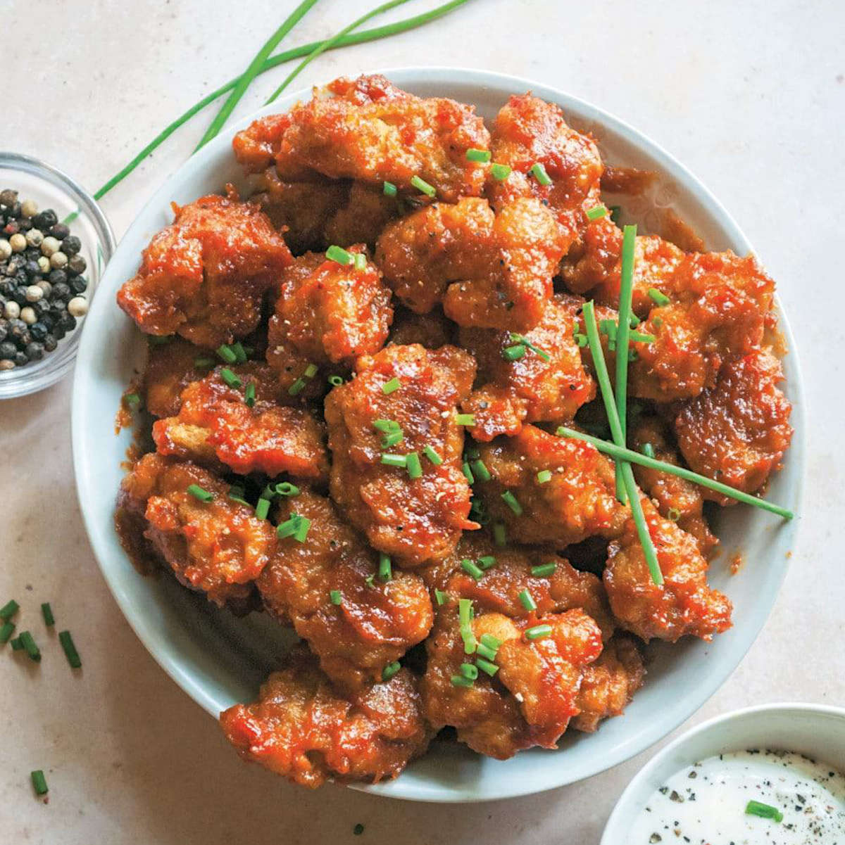 Seitan wings piled on a platter, topped with sliced chives.