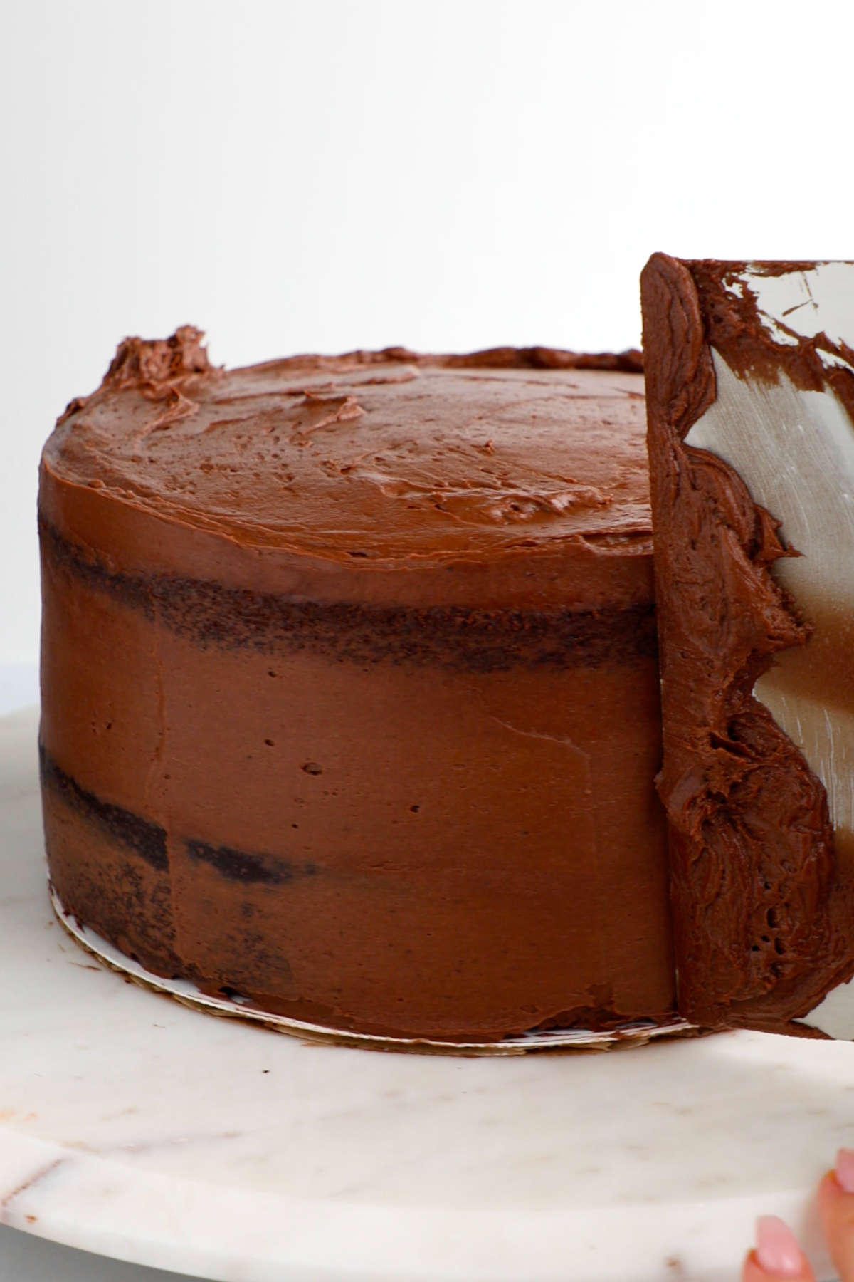 A cake on a turntable with frosting being smoothed by an icing smoother.