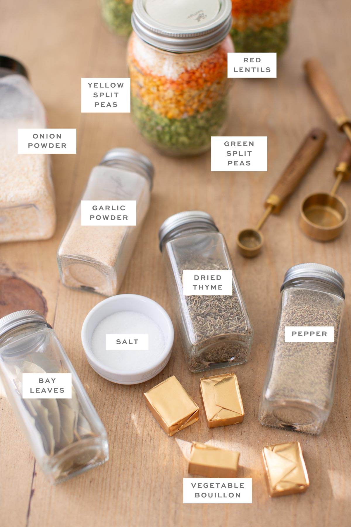 Gathered ingredients for this soup in a jar recipe including a jar filled with dried split peas and lentils, plus individual jars of seasonings scattered around.