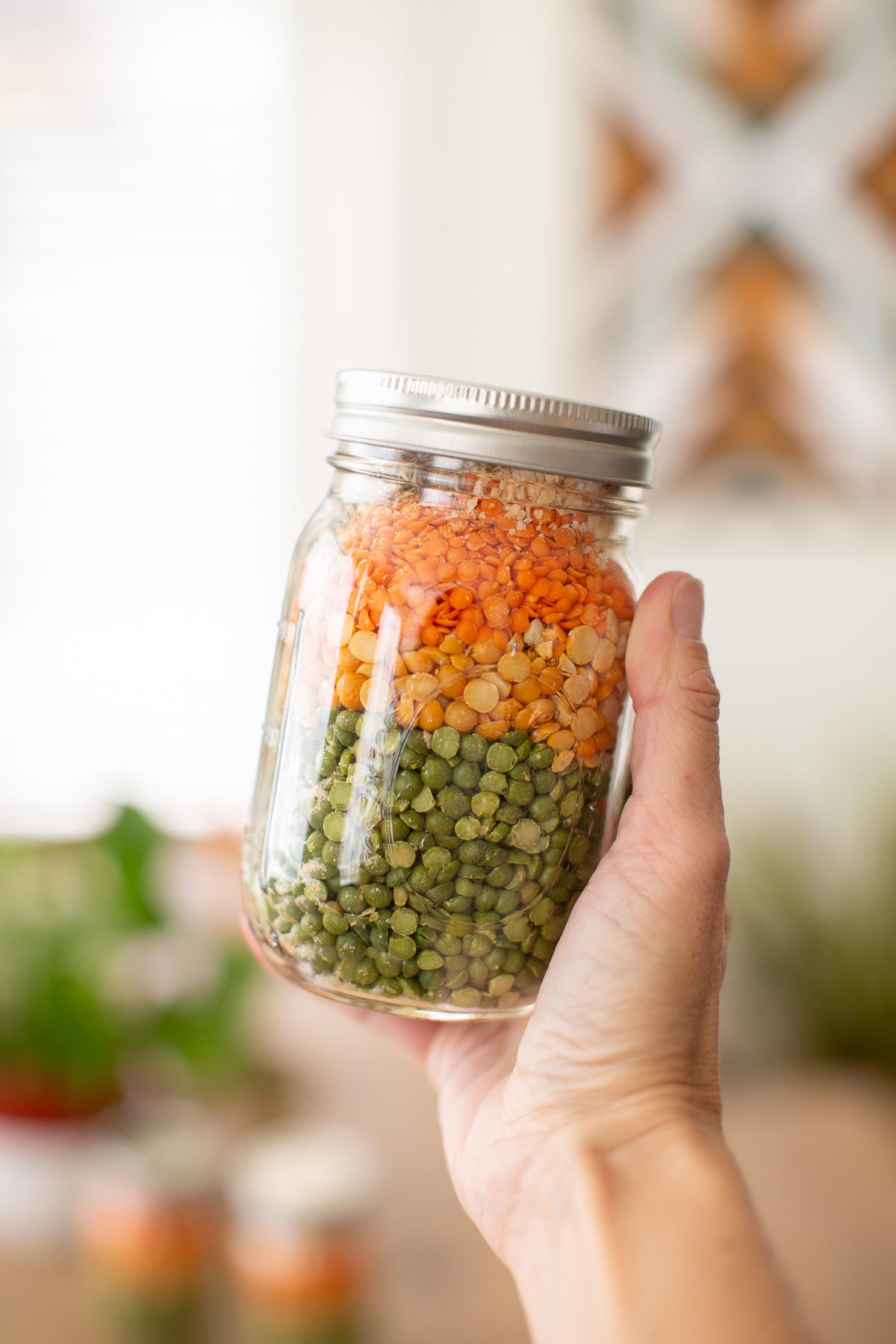 A hand holding up a mason jar filled with soup mix.