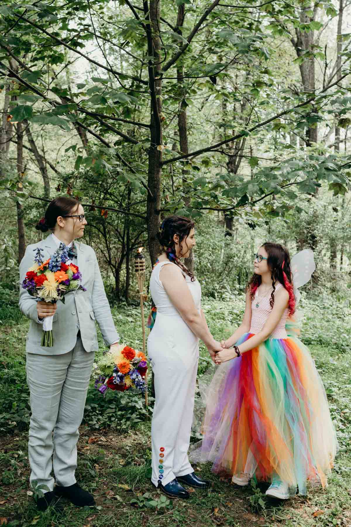 Bride reading vows to her stepdaughter in woodland rainbow ceremony.