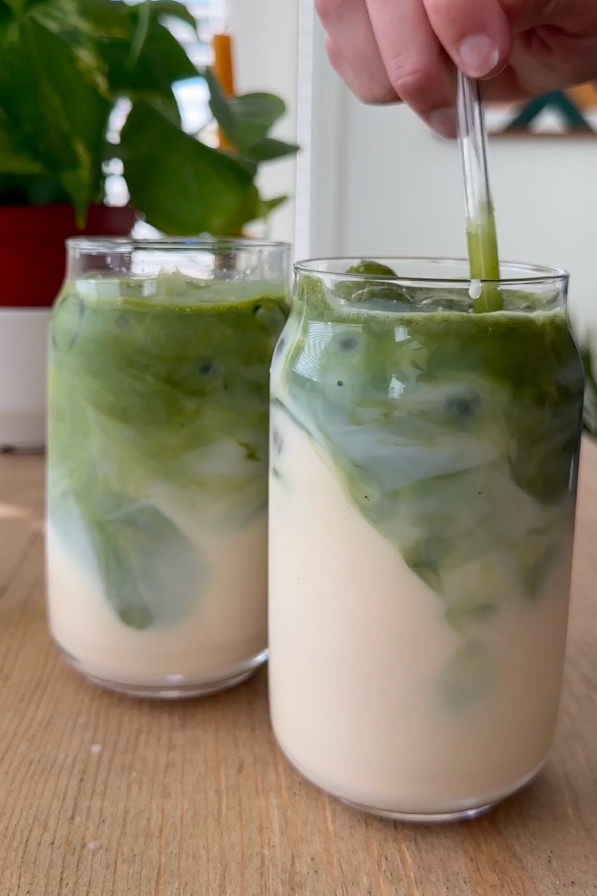 The prepared iced matcha lattes in glasses, stirred with a glass straw.