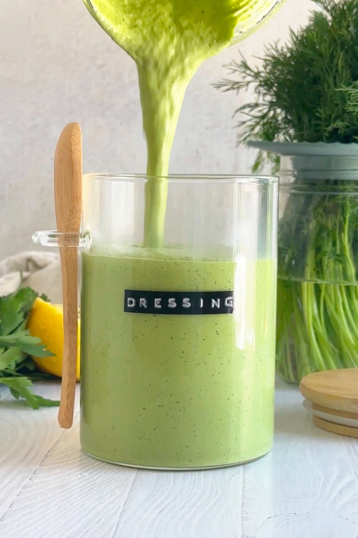 Green goddess dressing being poured from the blender pitcher into a sealable glass container.