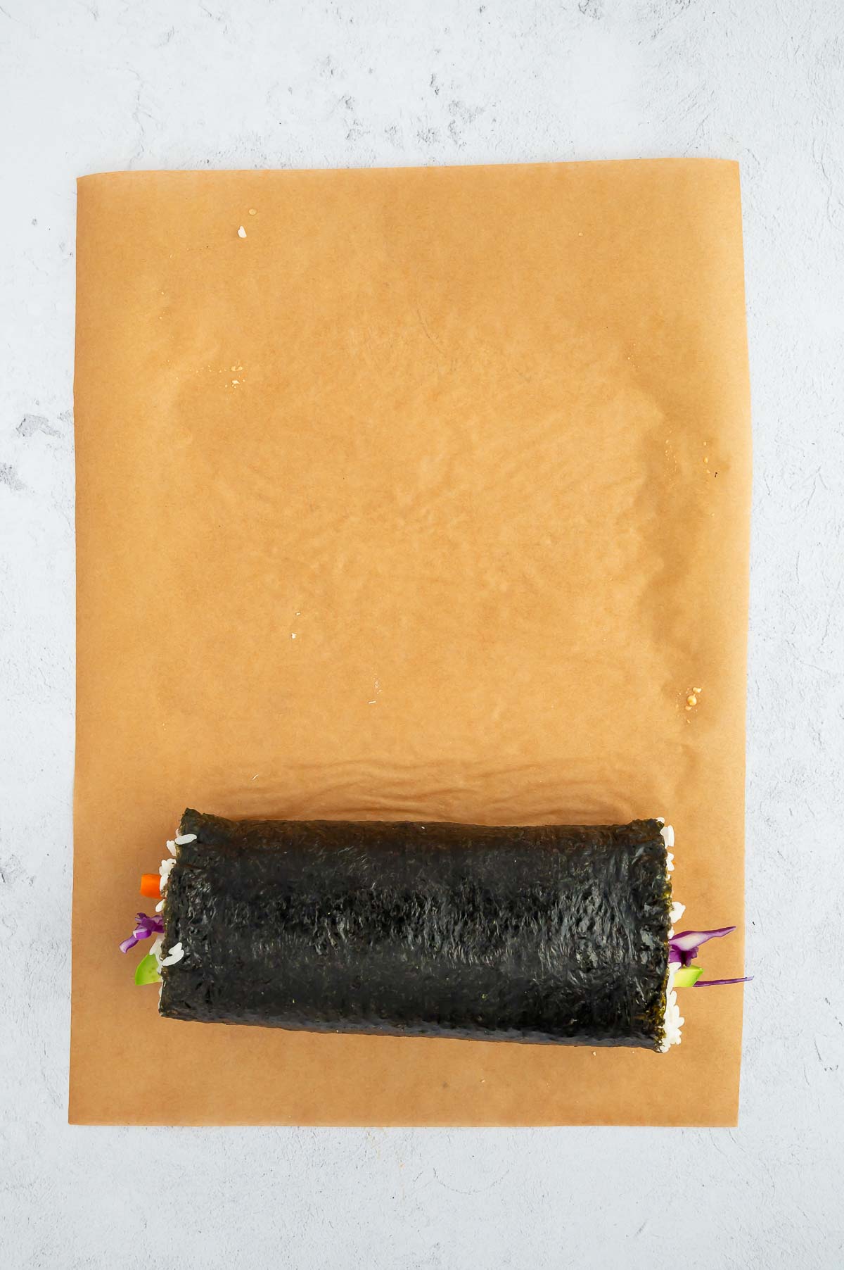 A fully rolled tofu sushi wrap sitting on parchment paper, filled with rice and veggies, ready to slice and serve.
