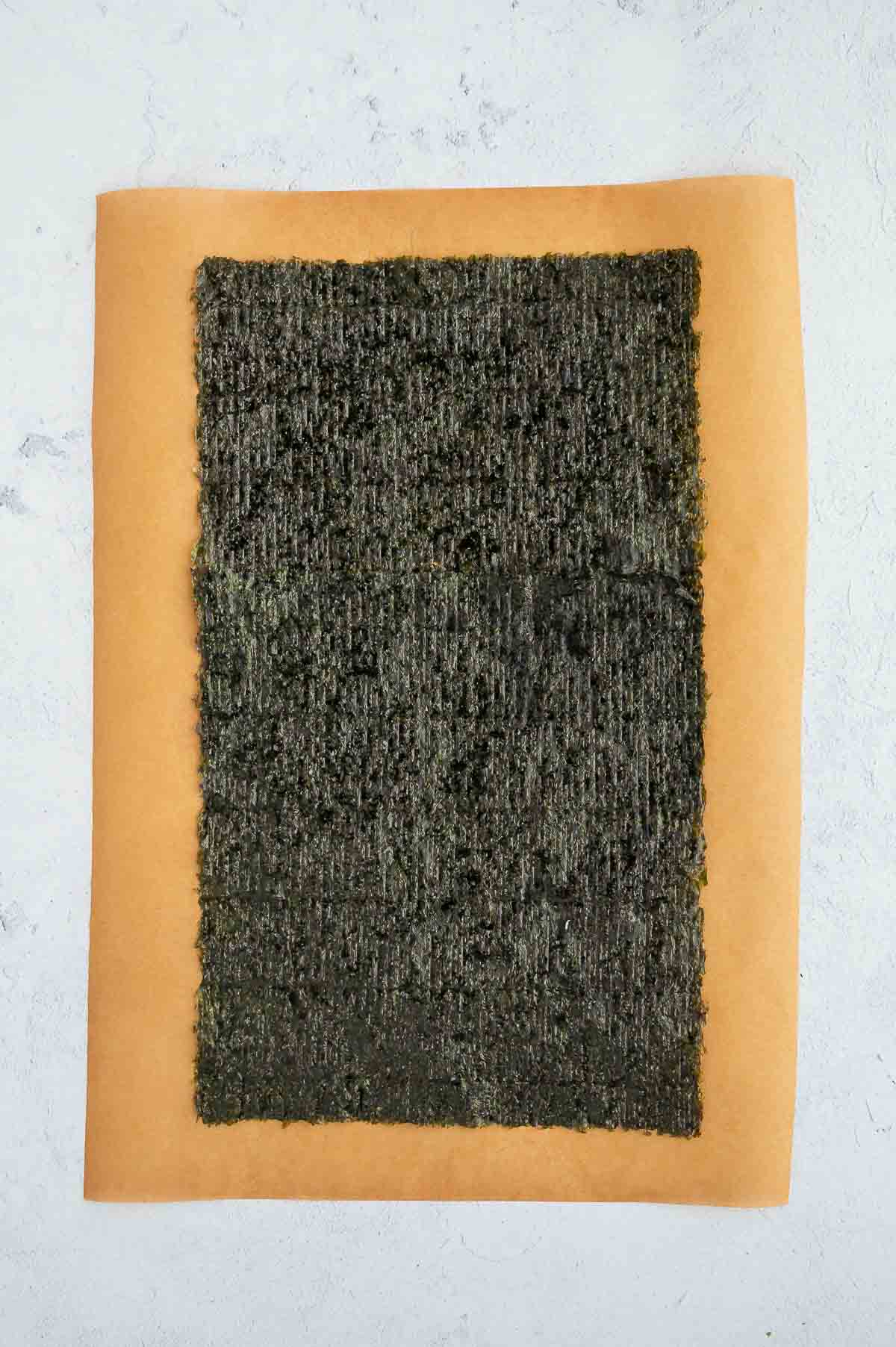 A single nori sheet placed on parchment paper, prepped and ready for making a tofu veggie sushi roll.