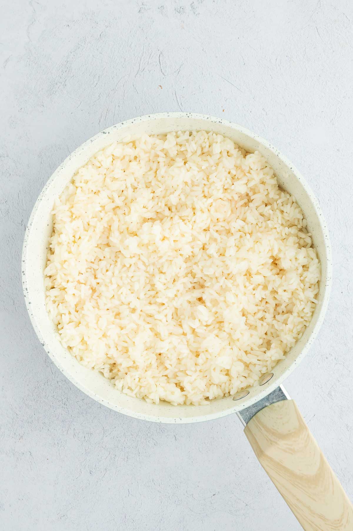 A pot of cooked seasoned sushi rice, fluffed and ready to use as the base for a homemade sushi burrito.