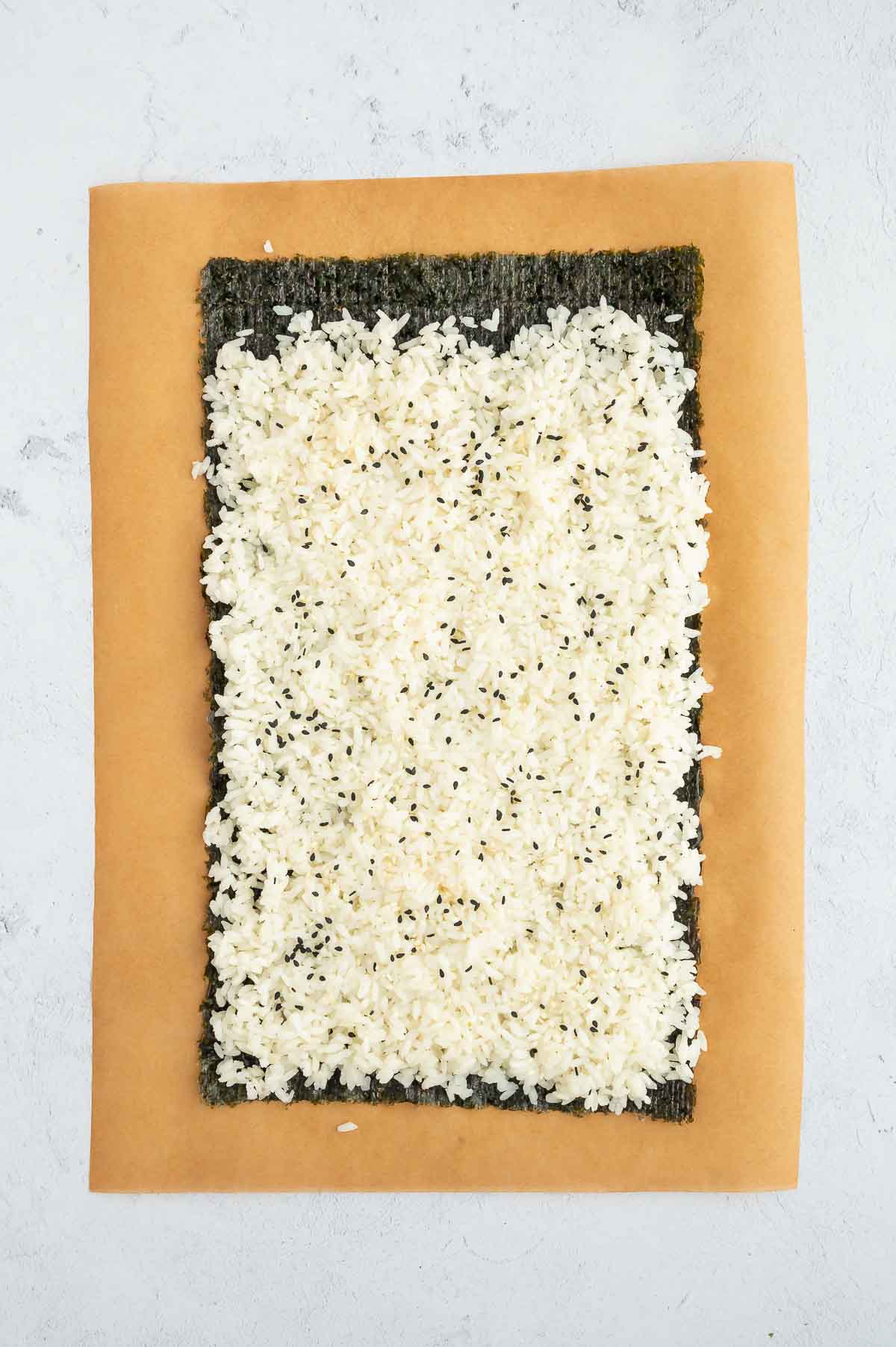 A sheet of nori topped with seasoned sushi rice and sprinkled with black sesame seeds, ready to be filled.
