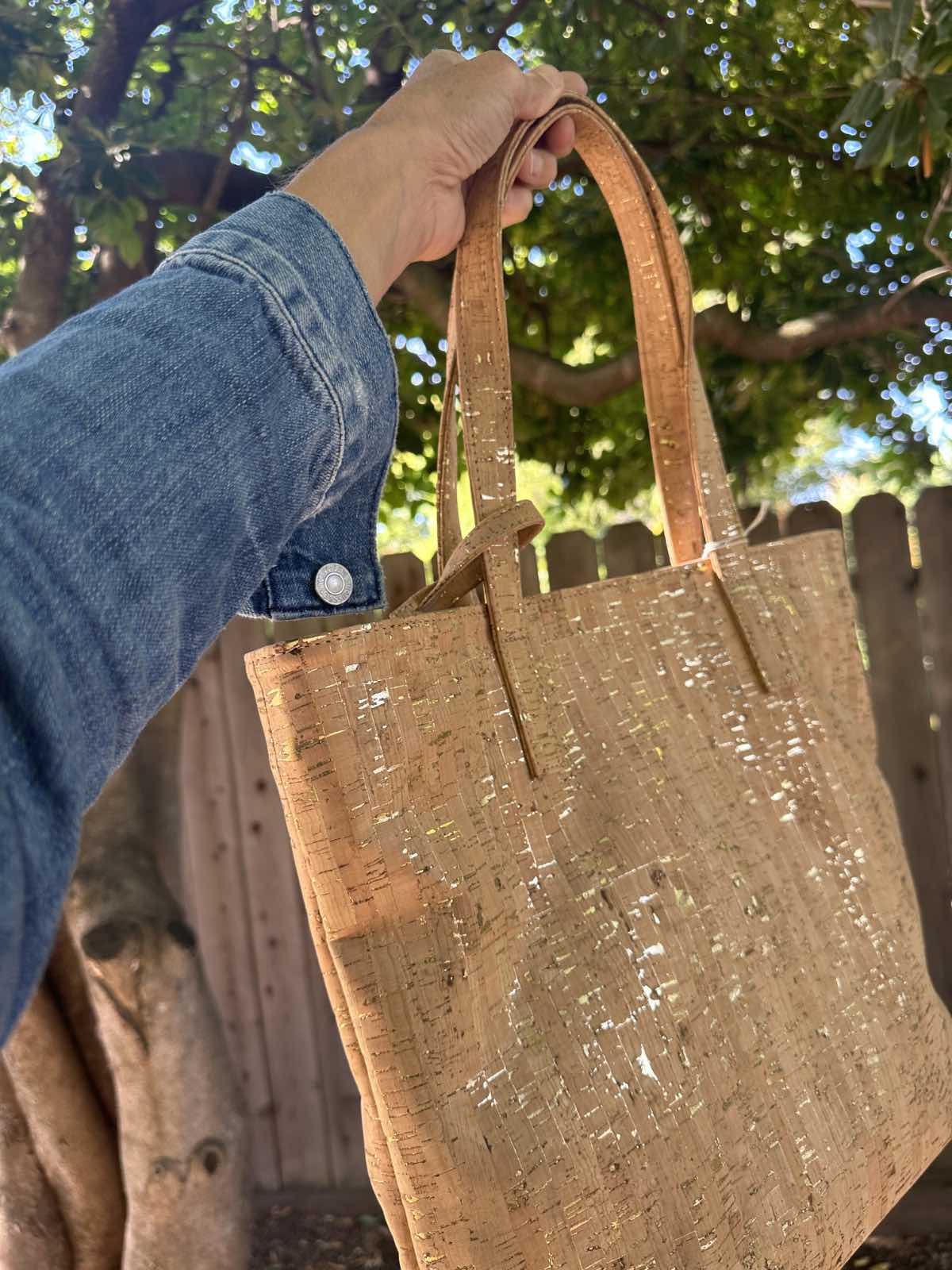 Woman holding out a gold speckled cork handbag from the vegan bag brand, Svala