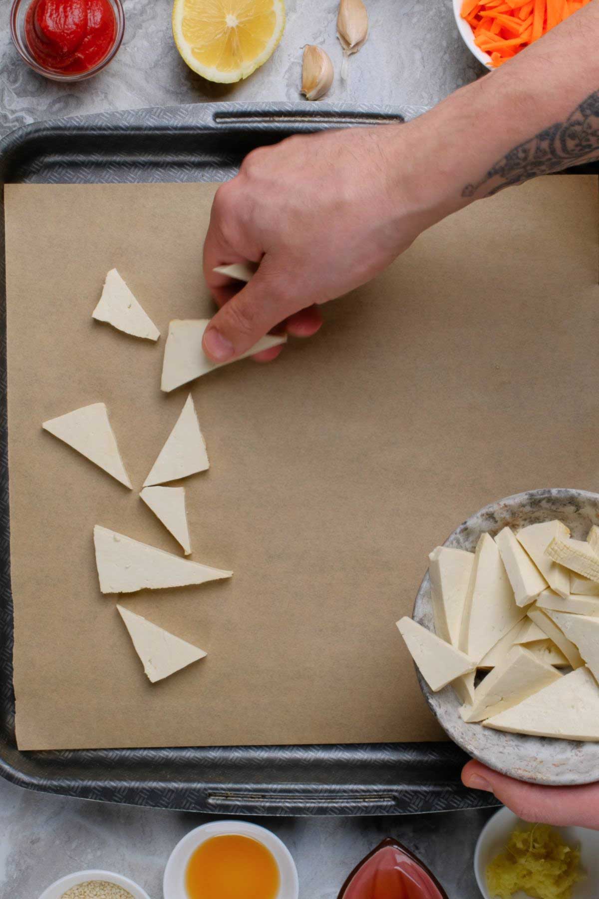 Tofu triangles being placed on a baking sheet.