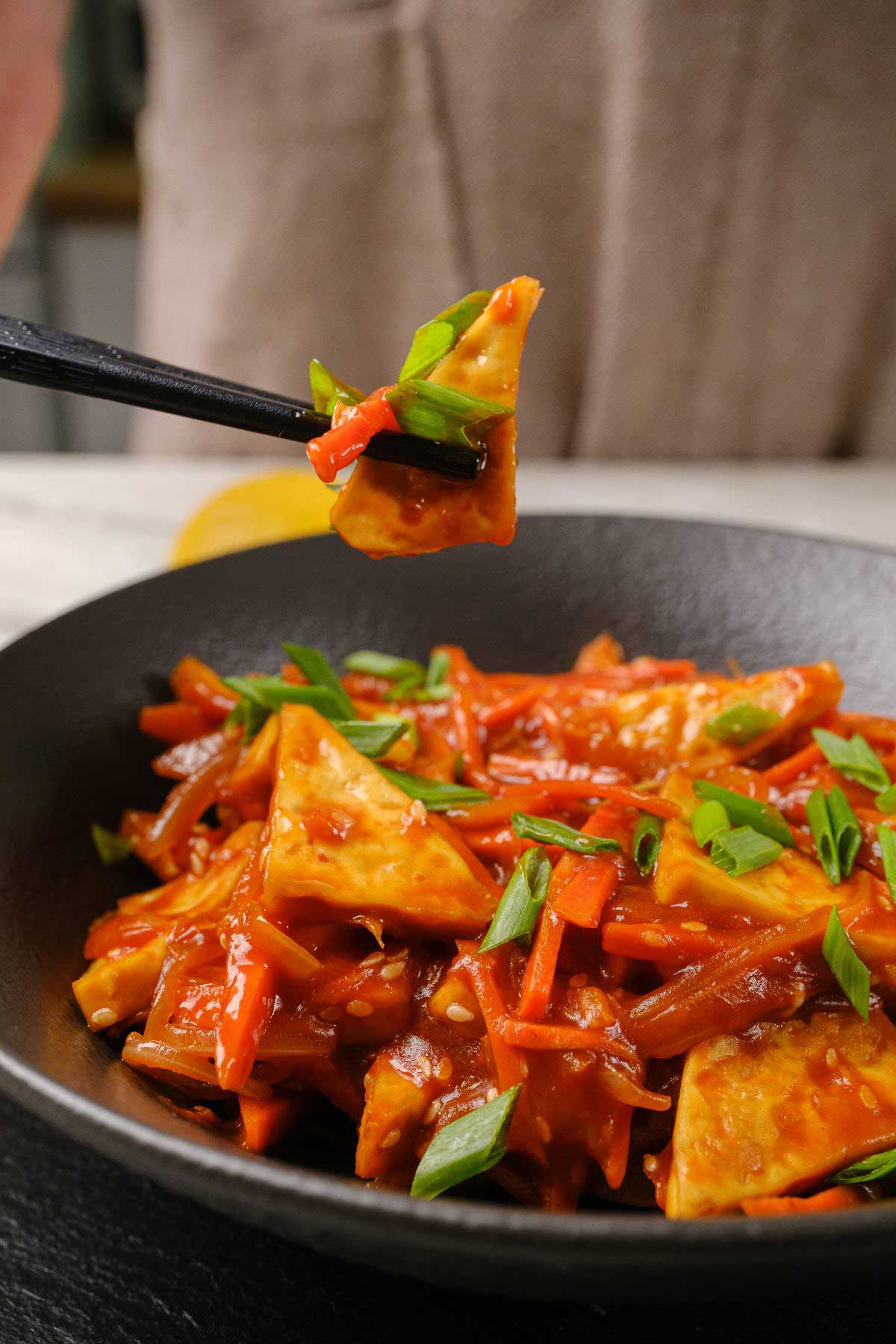 A chopstick holding up a piece of sweet and sour tofu.